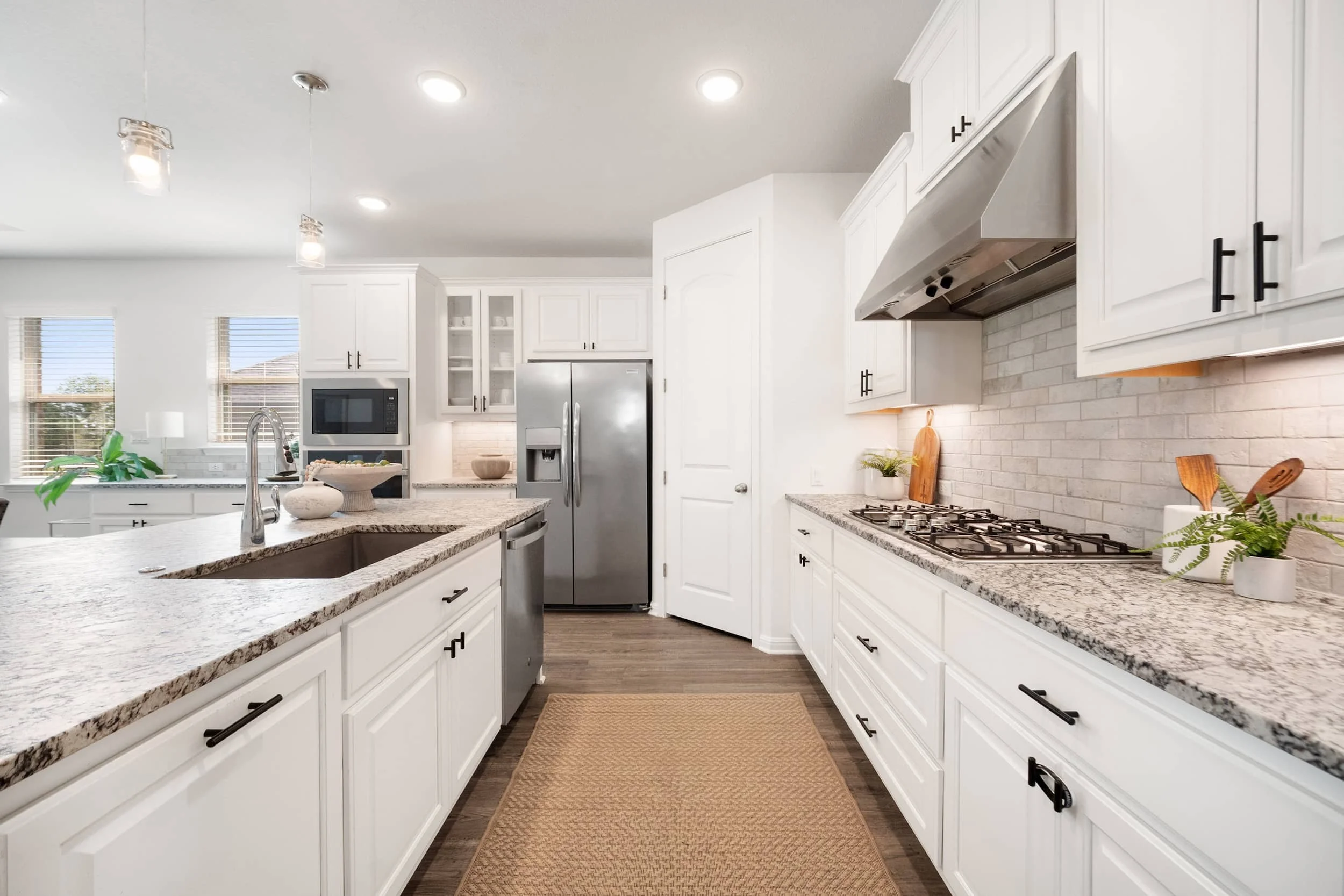 Bright Austin kitchen staging featuring a large granite island, stainless appliances, subway backsplash, and black hardware.