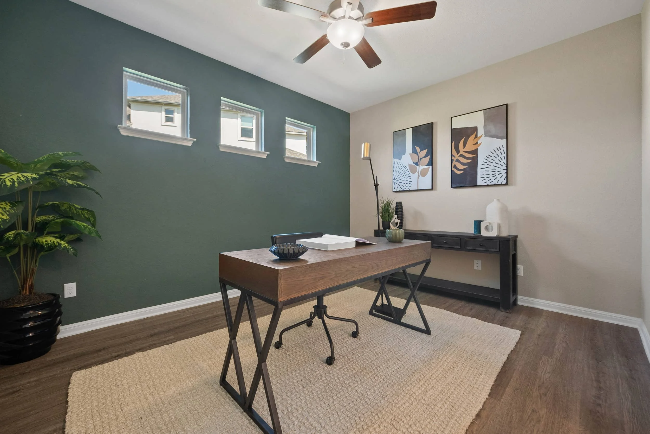 Staged home office in Austin with wood desk, black metal base, green accent wall, woven rug, curated decor, bright windows.