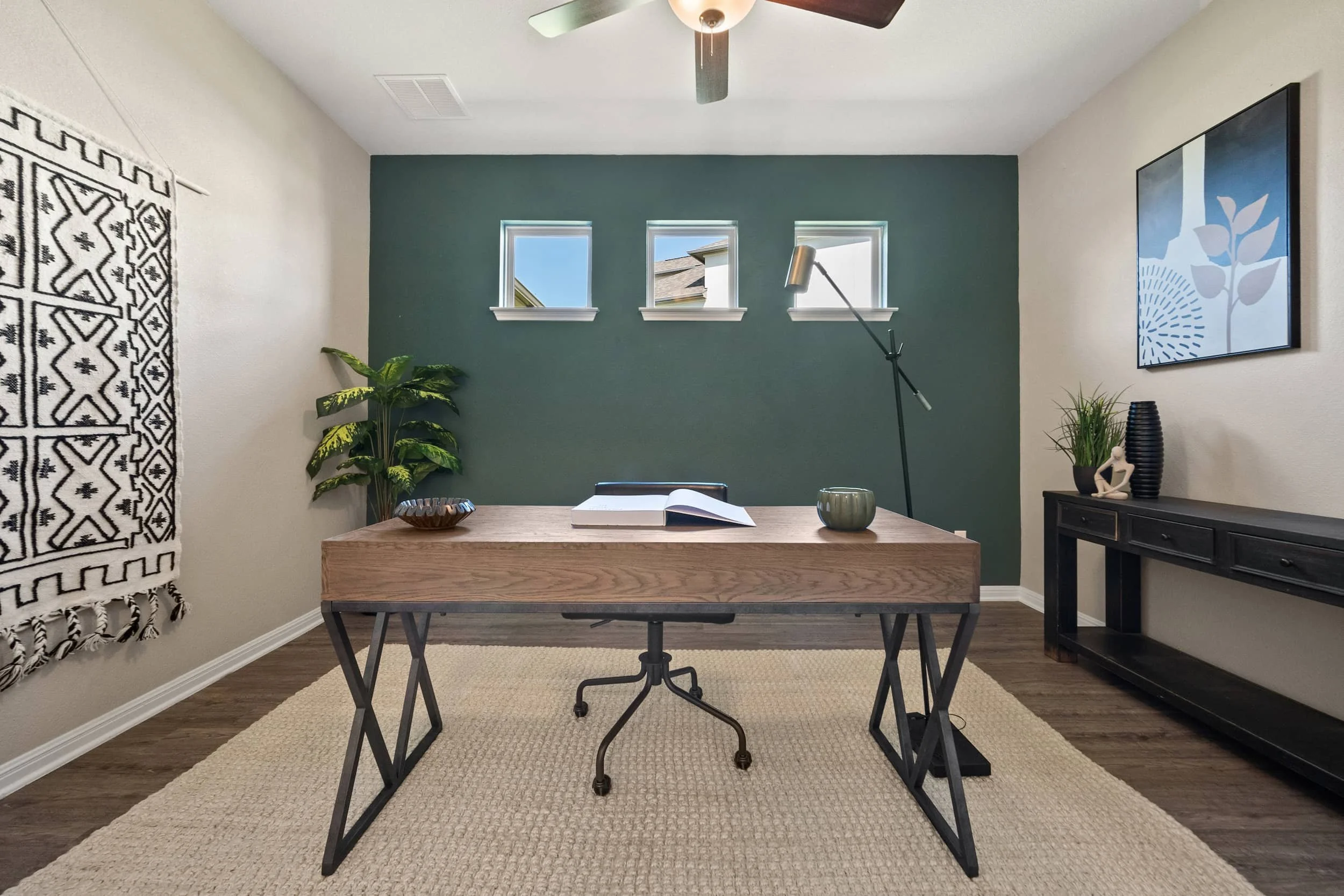 Modern staged kitchen with wood table black metal accents green accent wall, neutral rug minimalist decor, natural light.