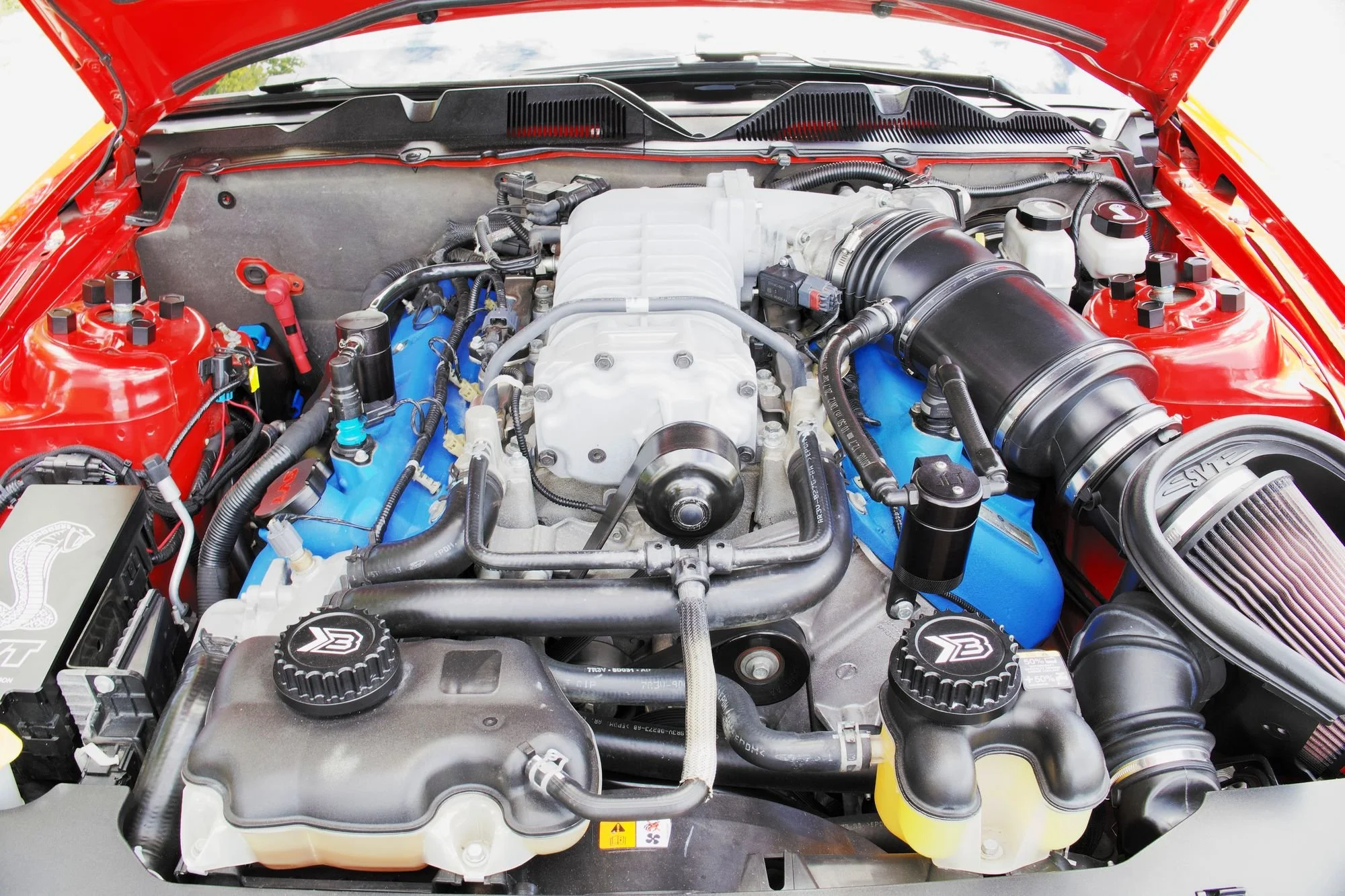 Engine bay of a red Shelby GT500 with black billet shock tower caps installed on both shock towers