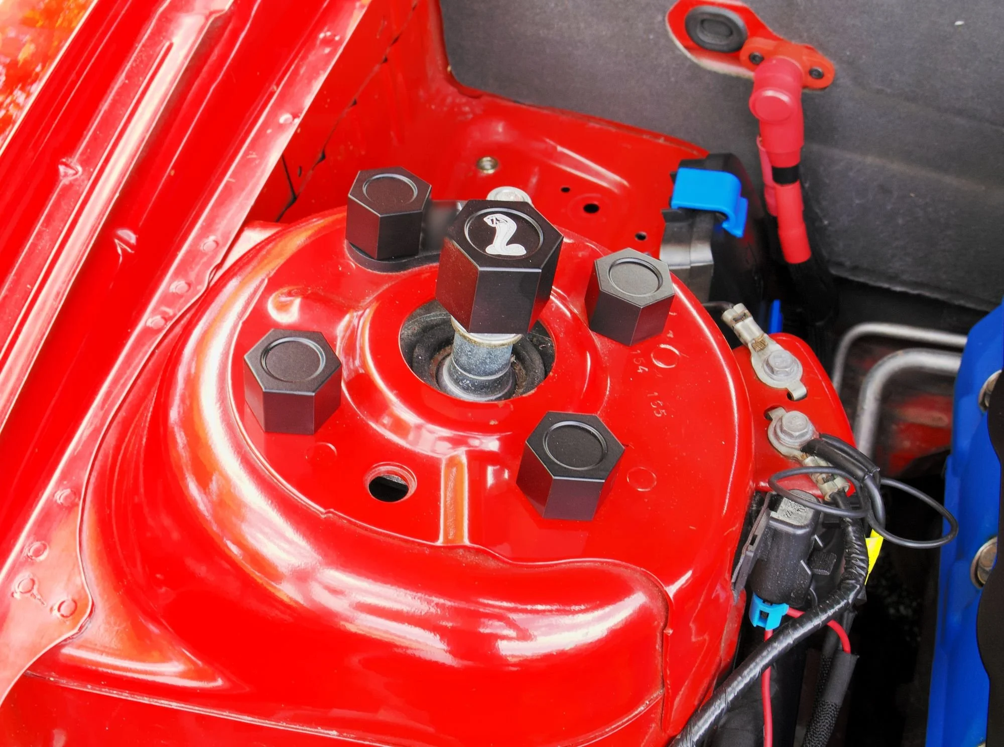 Black billet shock tower caps installed on the driver side shock tower of a red Shelby GT500, seen from above