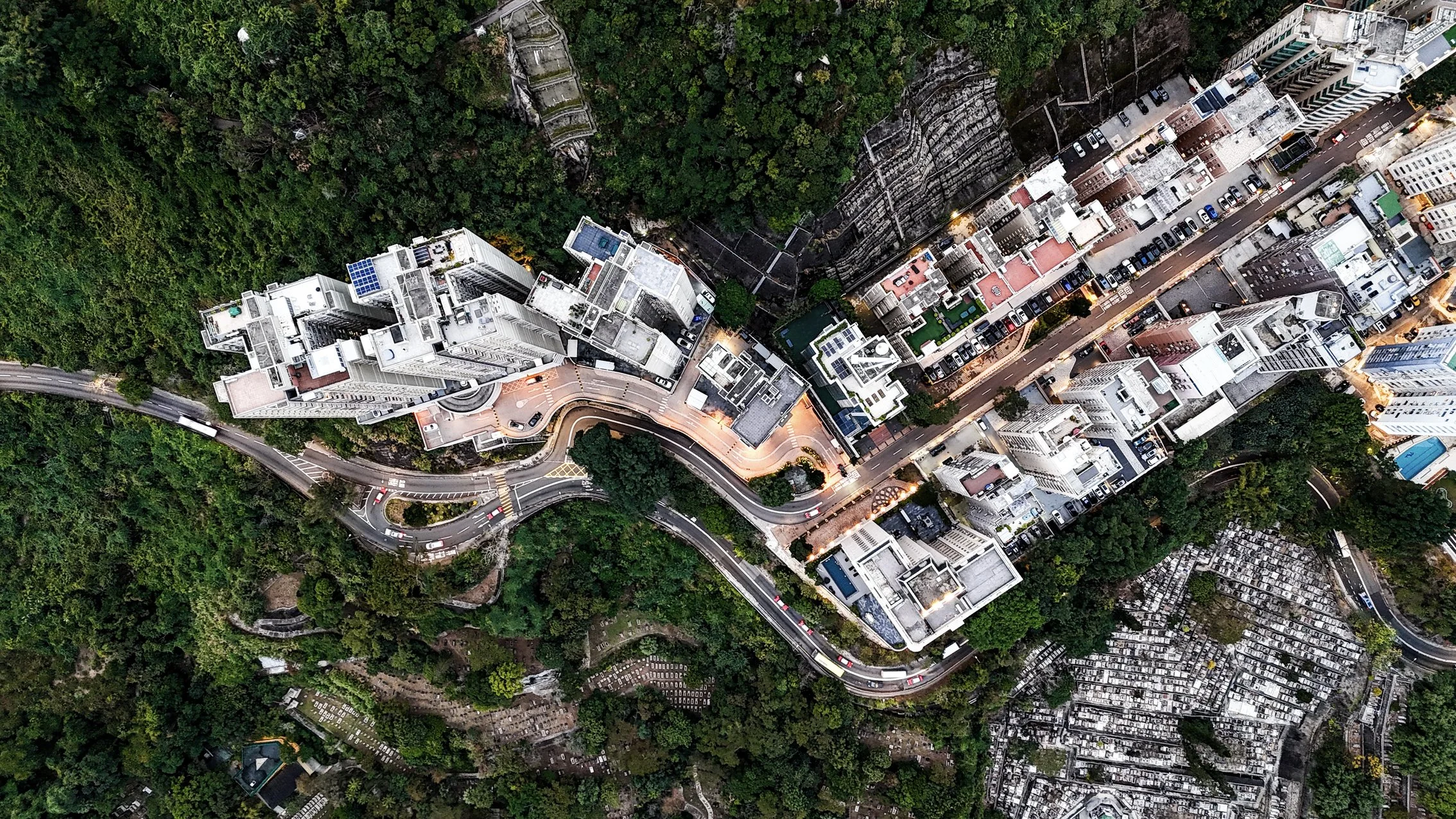 An aerial view of a city with high-rise buildings, winding roads, and surrounding green areas.