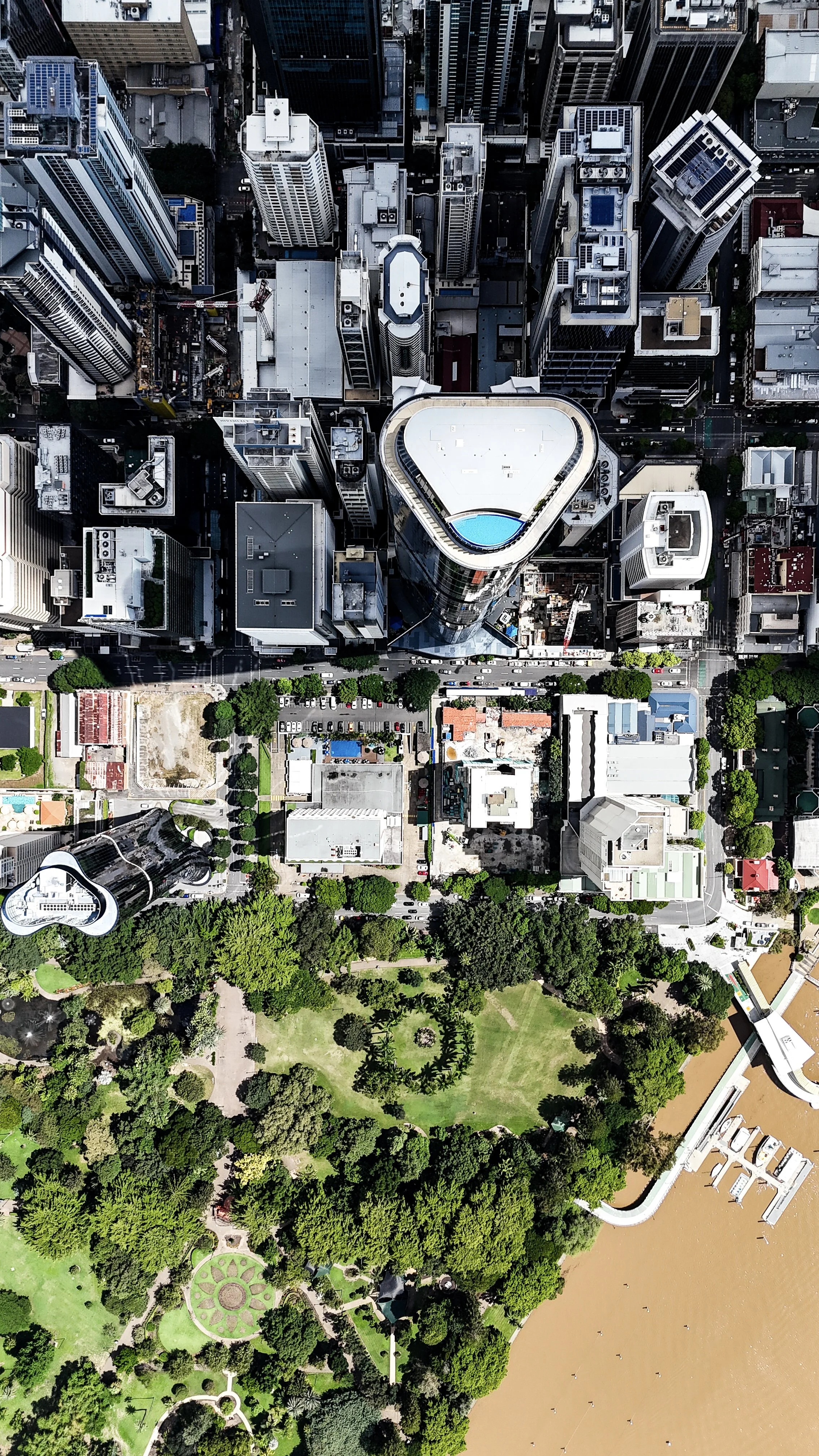 An aerial view of a cityscape showing high-rise buildings, a park with green trees, and a river with a marina.