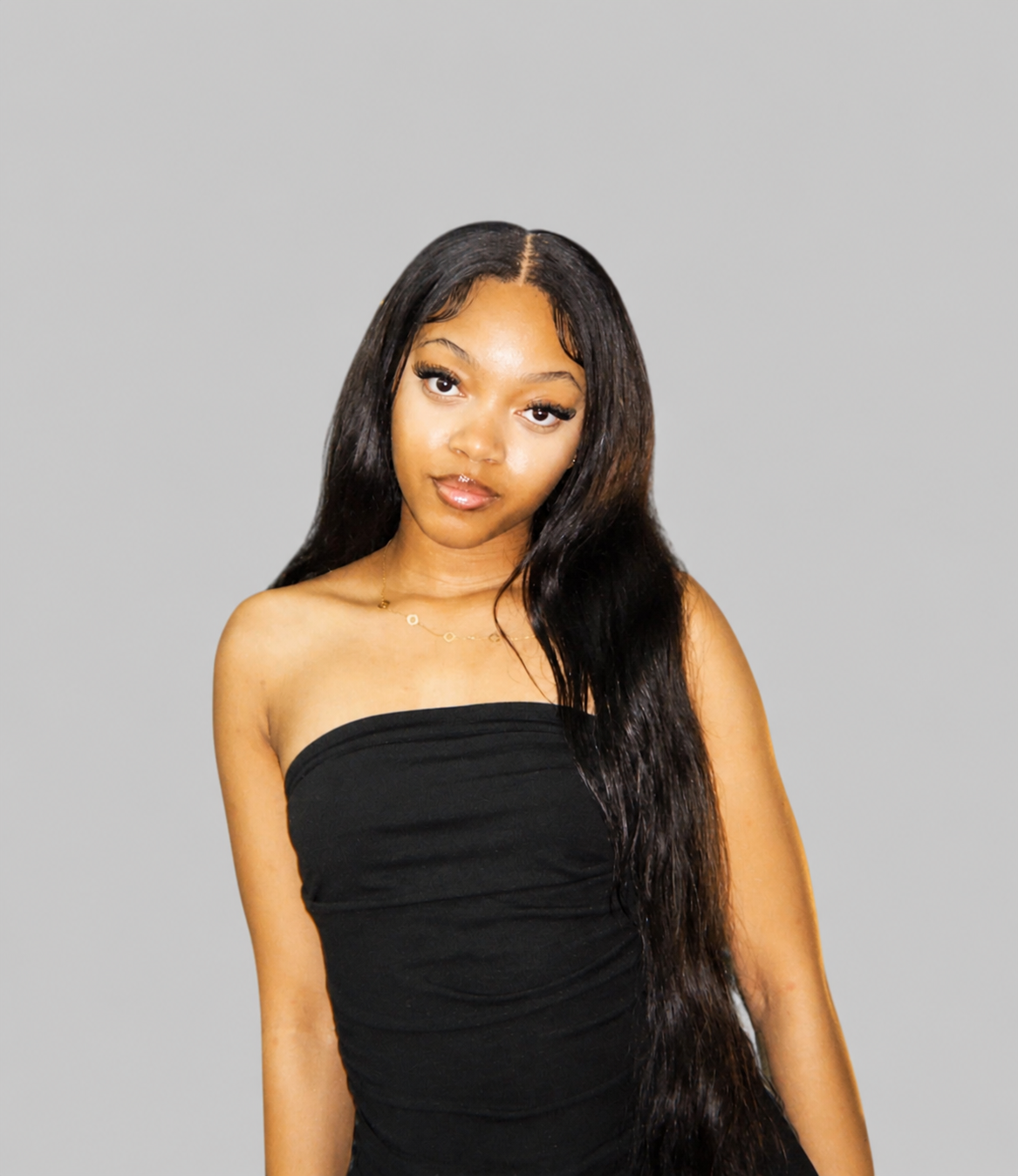 Young woman with dark, curly hair in a ponytail, wearing a black T-shirt with a logo that says 'We Act Together Siyanda Hadebe Foundation' and an image of a tree, standing against a plain white wall.