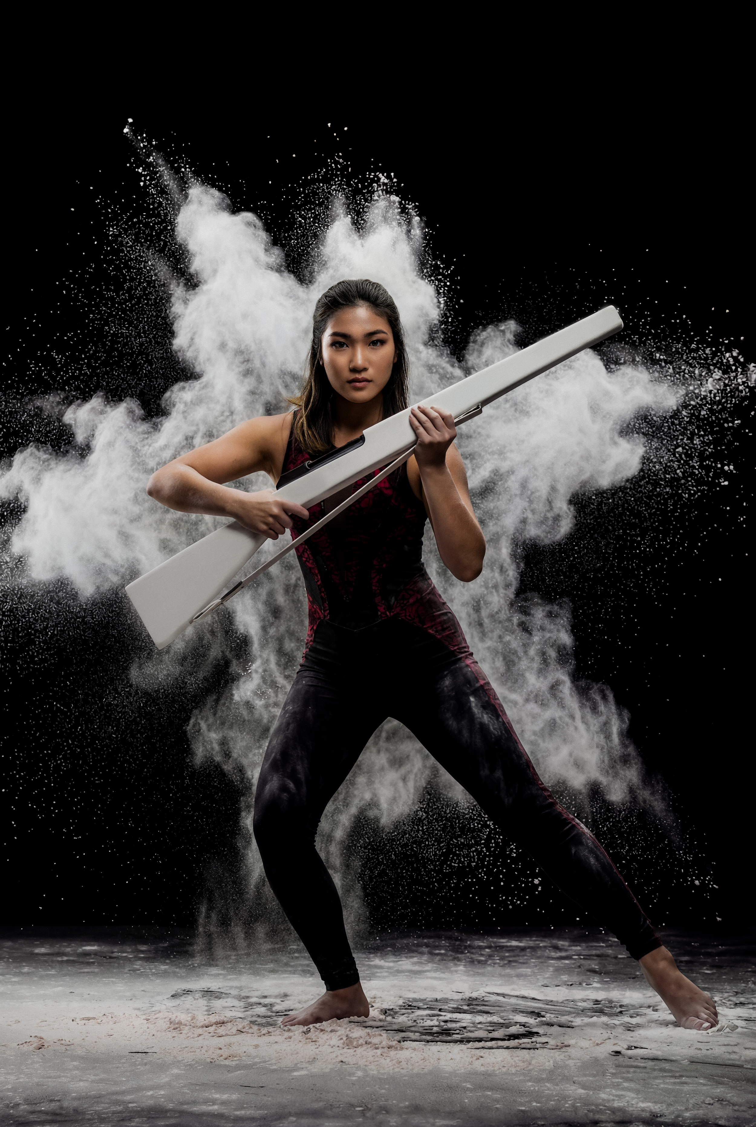 A woman holding a white rifle posing with dramatic smoke and dust effects against a black background.