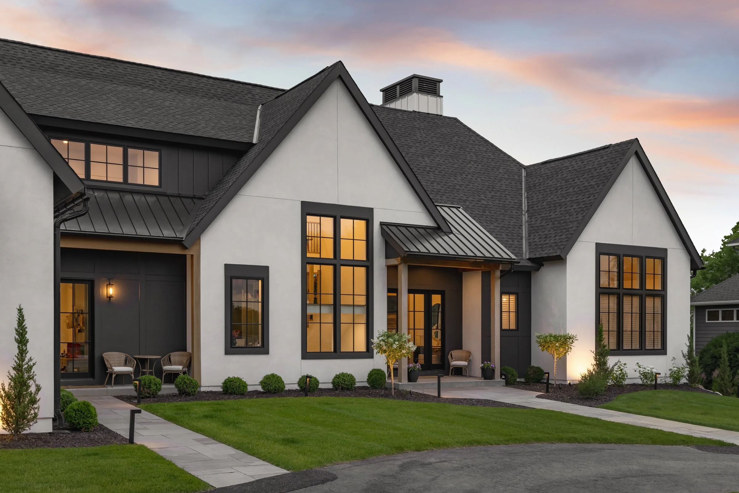 Modern house with large windows, black accents, and well-manicured lawn at sunset.