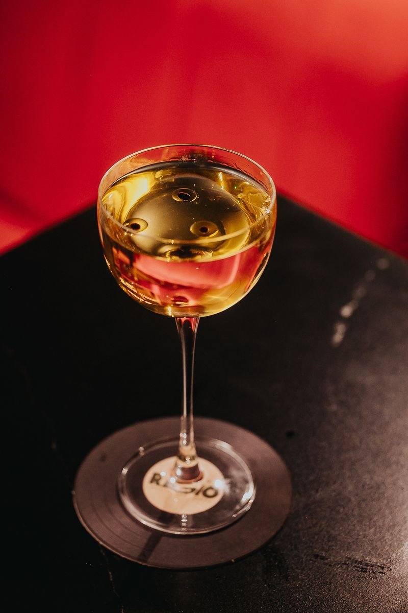 A glass of white wine on a black table against a red background.