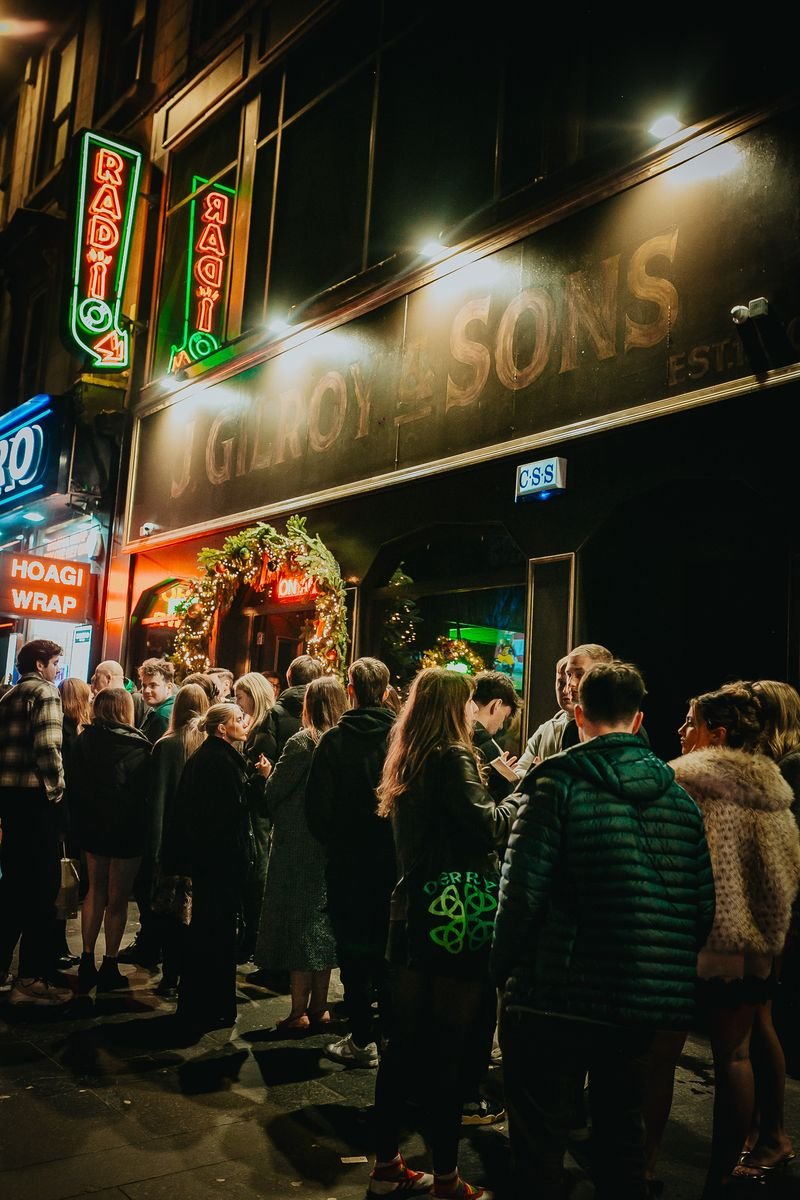 People line up outside the Globe and Son's restaurant at night, decorated with Christmas wreaths and lights.