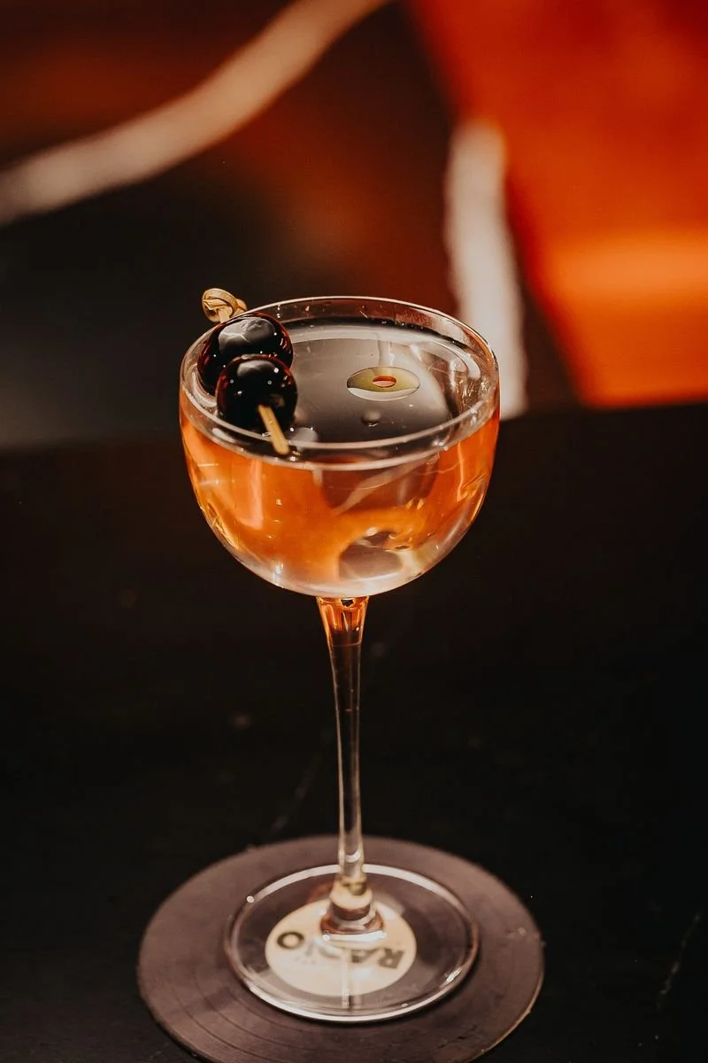 Cocktail in a coupe glass garnished with black cherries on a skewer