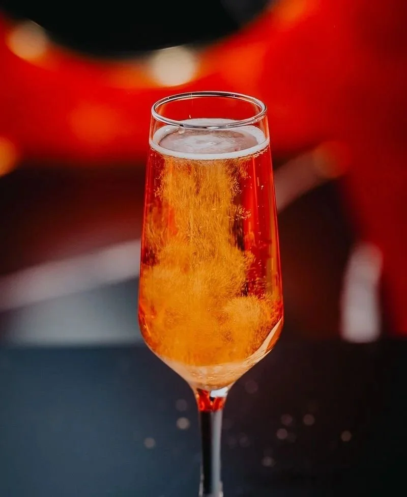 A glass of rosé wine with bubbles, against a blurred red background.
