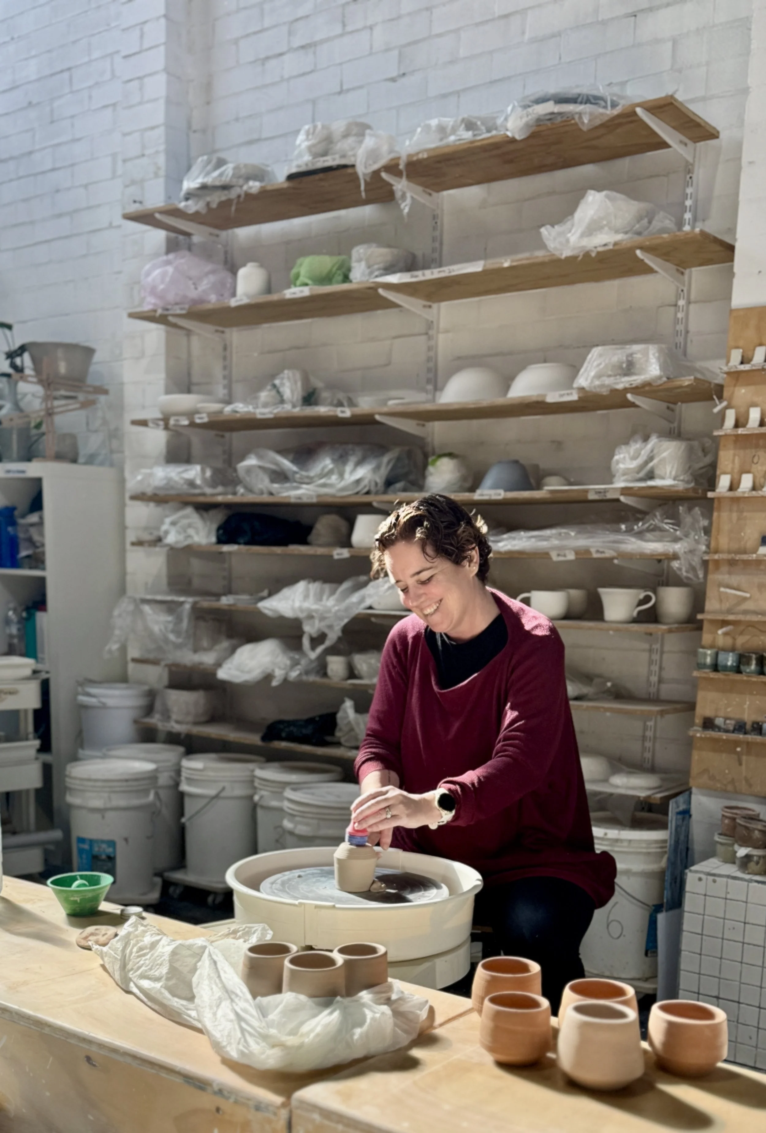 Shae at the pottery wheel in a beam of sunlight