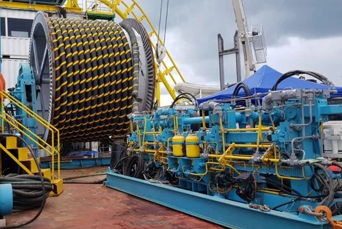 Oil drilling equipment on a platform, including a large coiled drilling pipe and machinery with blue and yellow components during daytime.