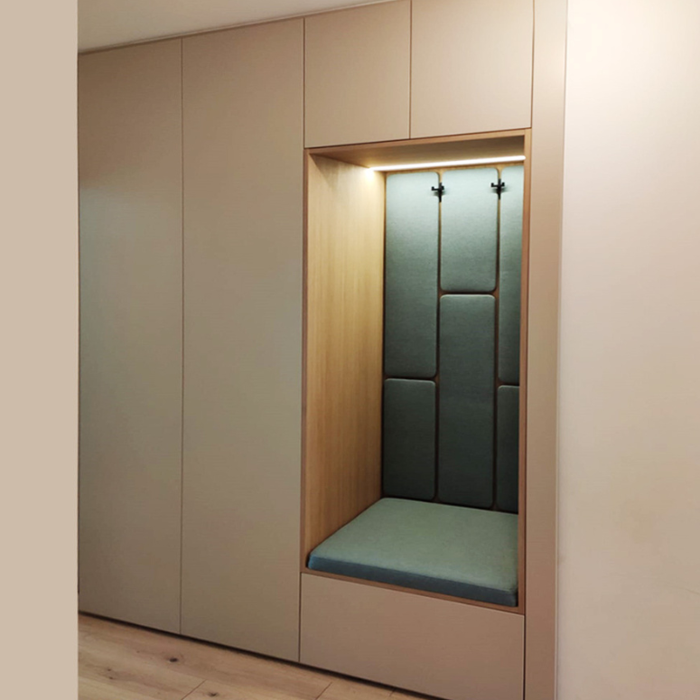 A modern built-in seating nook with cushioned backrest and seat, integrated into a wall with wood and neutral-colored panels, featuring overhead lighting.