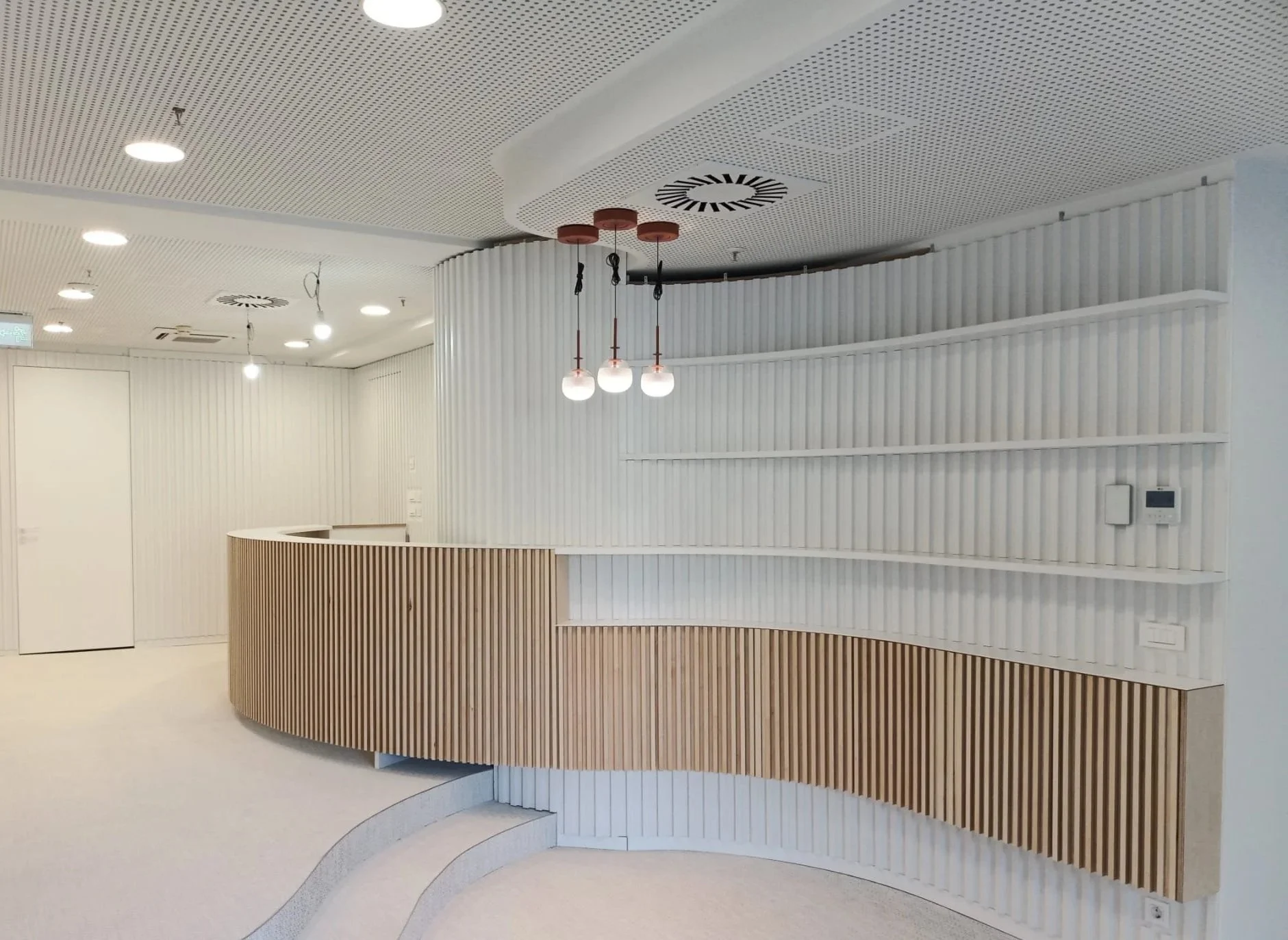 Modern reception or desk area with curved wooden and white paneling, pendant lights, and a white textured ceiling.
