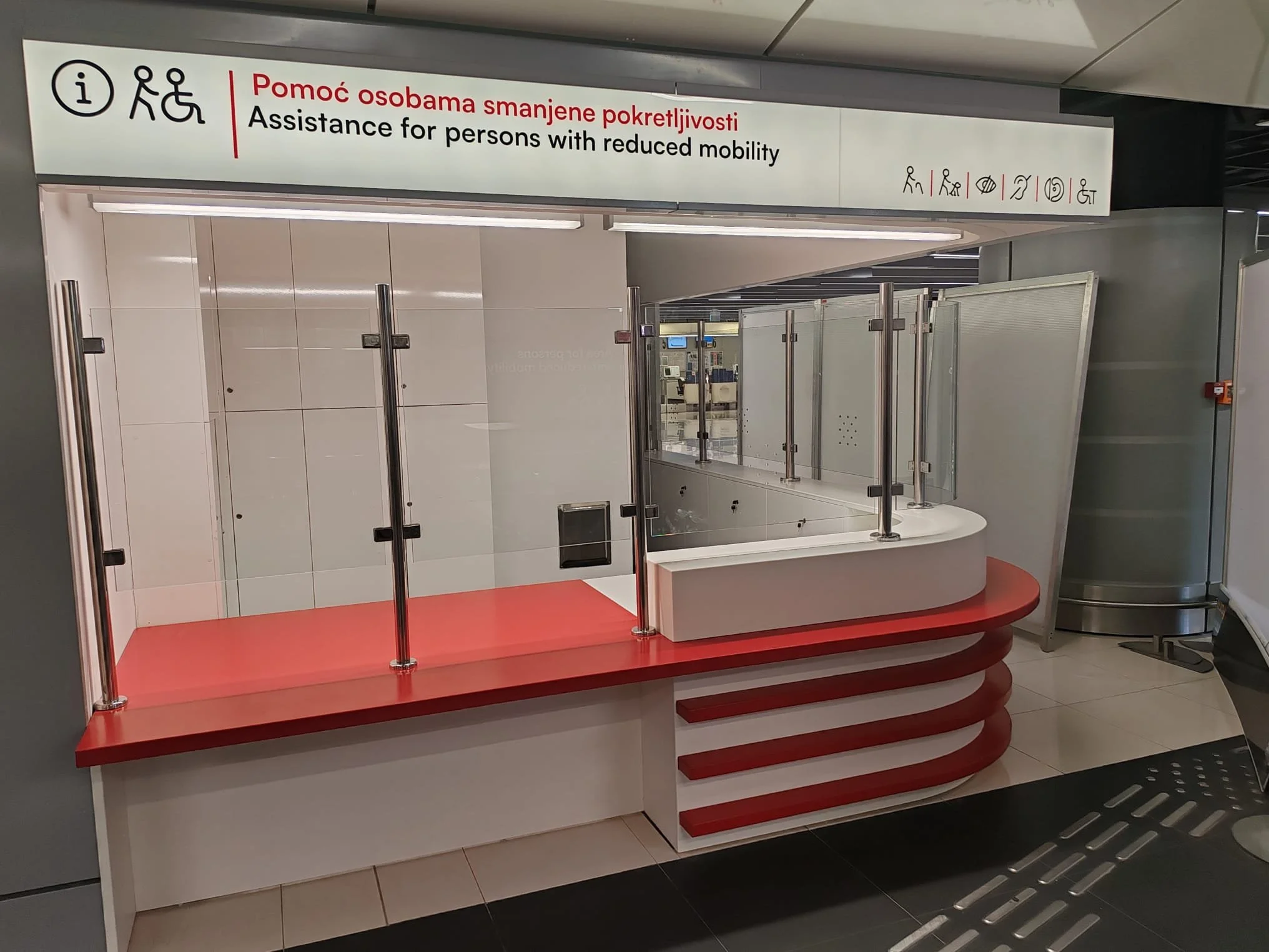 Assistance kiosk for persons with reduced mobility at an airport, with a sign in both Polish and English indicating the service.