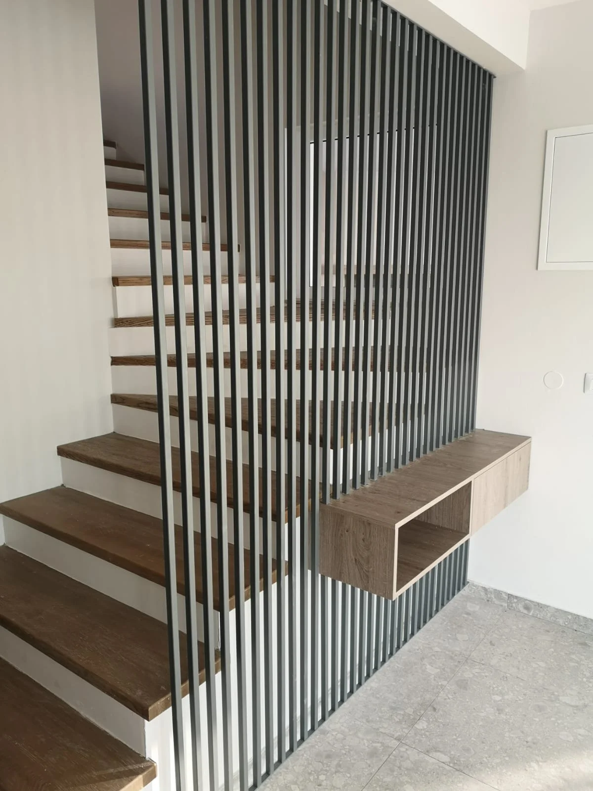Modern staircase with wooden steps and black vertical metal rods, featuring a built-in wooden storage unit underneath.