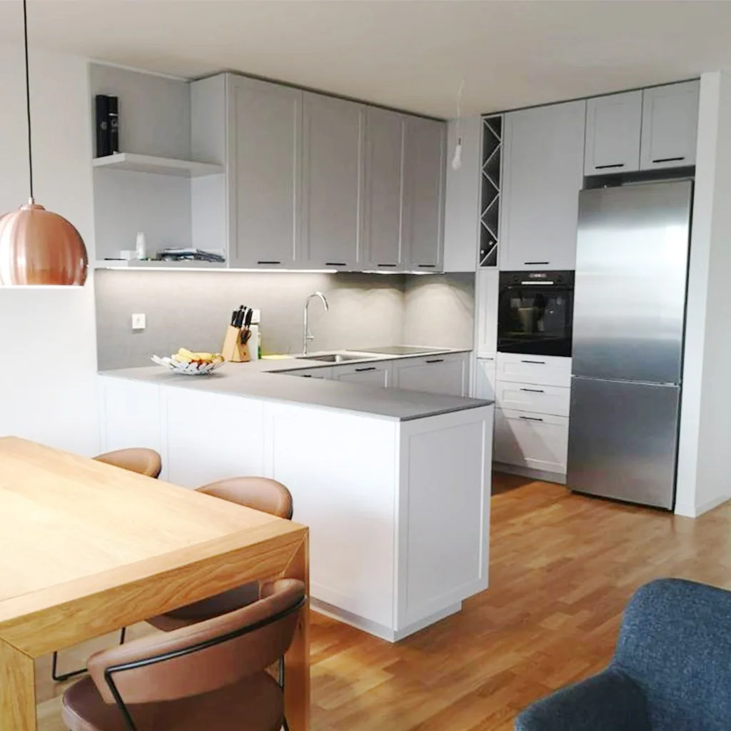 Modern kitchen with white cabinets, stainless steel appliances, and a wooden dining table with beige chairs.
