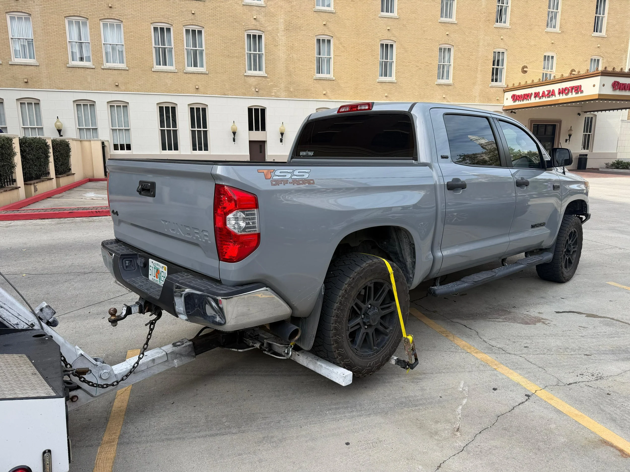 A beige car being loaded onto a red tow truck with a wheel lift.