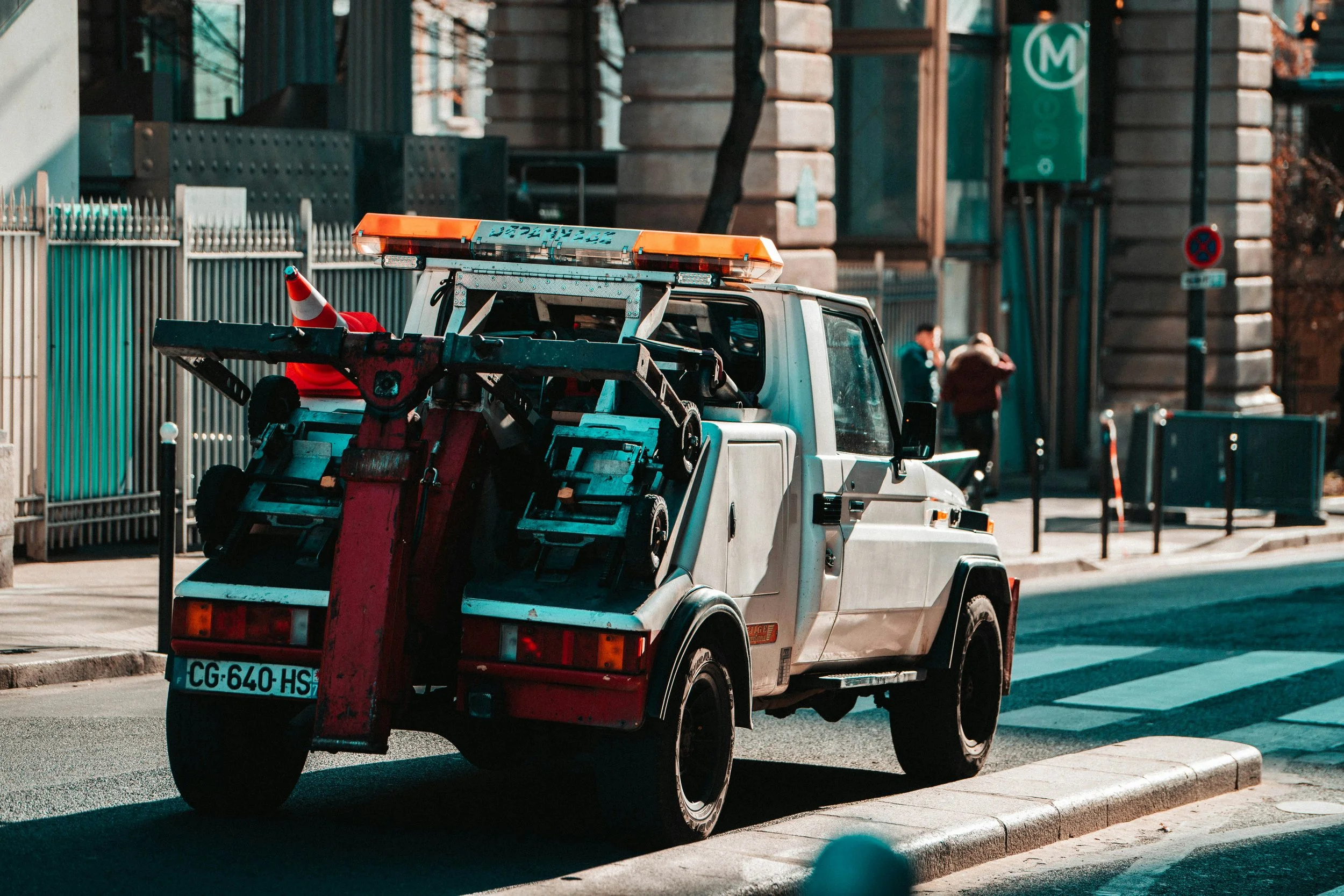 A white tow truck parked on the side of the road, transporting a red compact car on a yellow hydraulic flatbed.