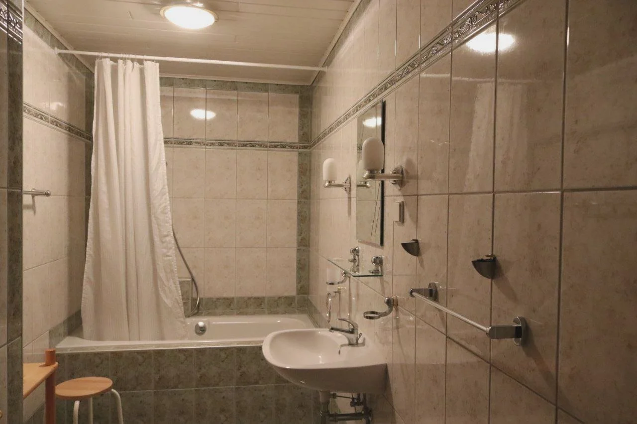 Badezimmer mit Dusche, Waschbecken, Spiegel, Handtuchhaltern und Badutensilien.