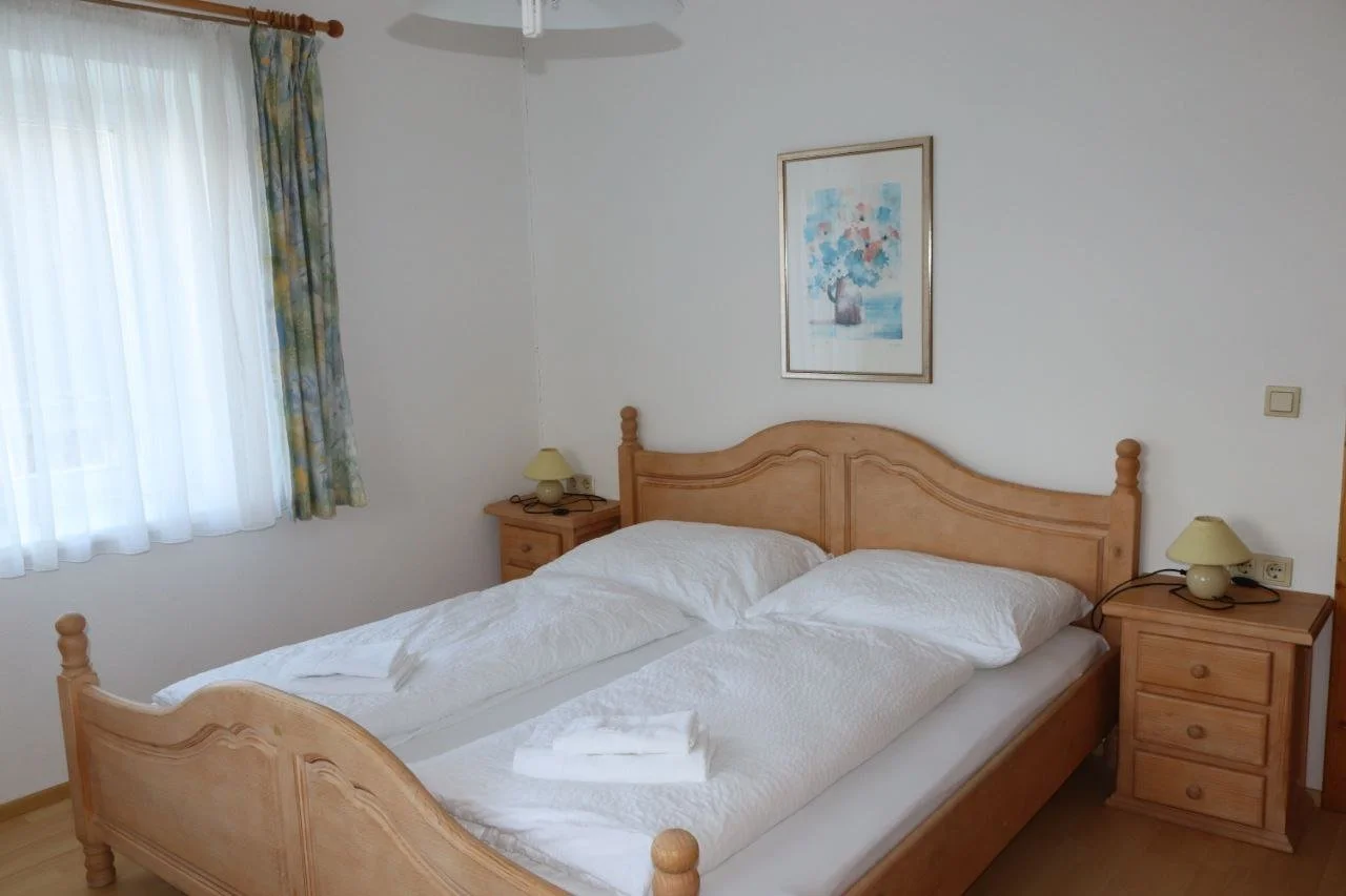 Ein Hotelzimmer mit einem Doppelbett, Holzmöbeln, einem Fenster mit Vorhängen, einem Wandbild und Nachttischlampen.