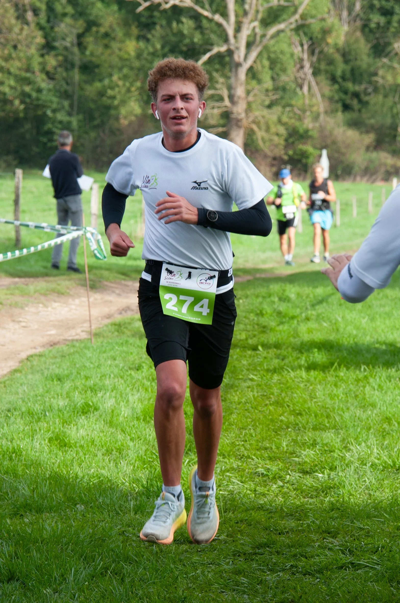 Jeune homme courant lors d'une course en extérieur, portant un t-shirt blanc, un numéro de course 274, et des écouteurs.
