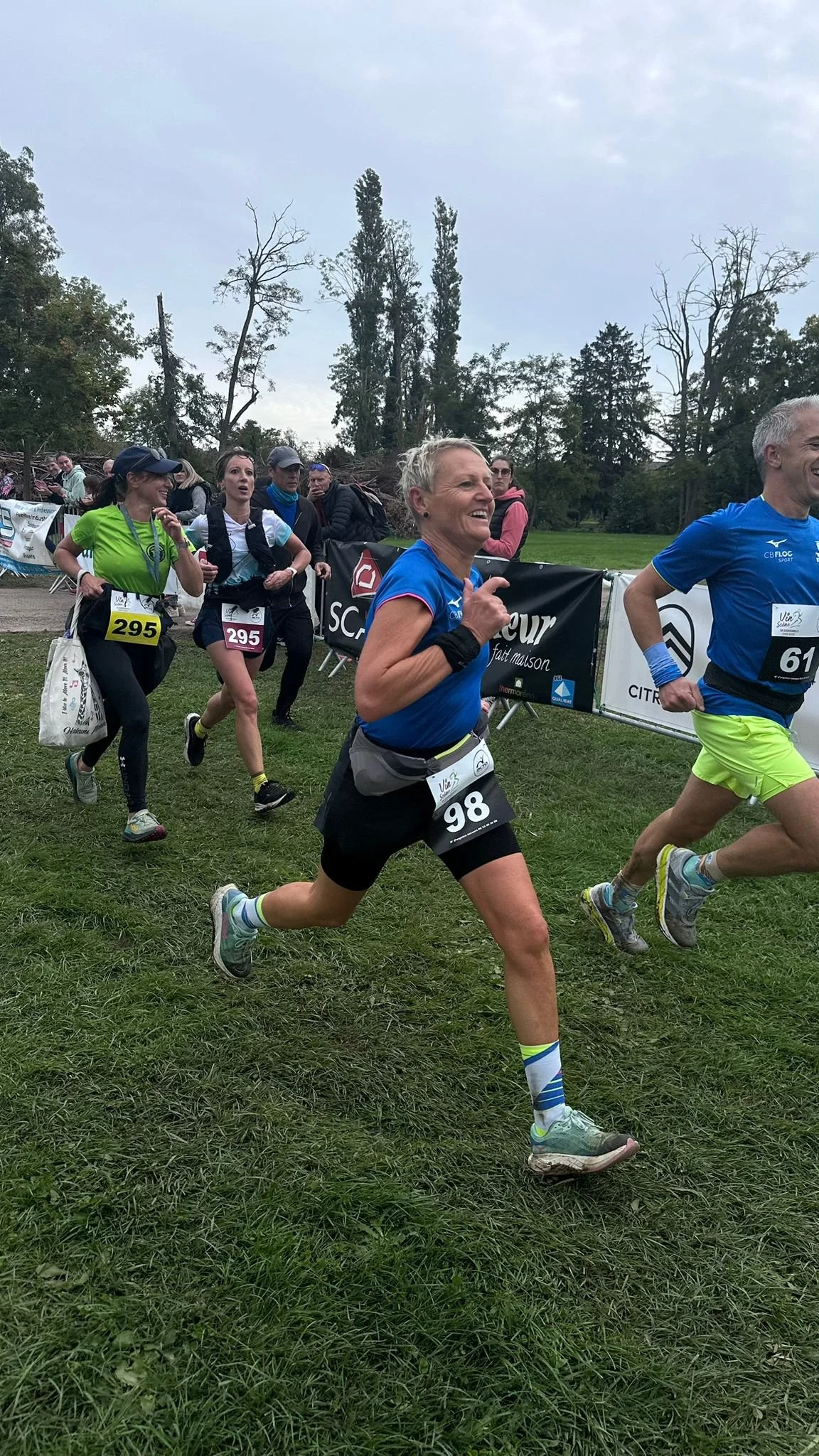 Des coureurs participent à une course en plein air sur de l'herbe. Écure, sourire et défilé d'arbres en arrière-plan.