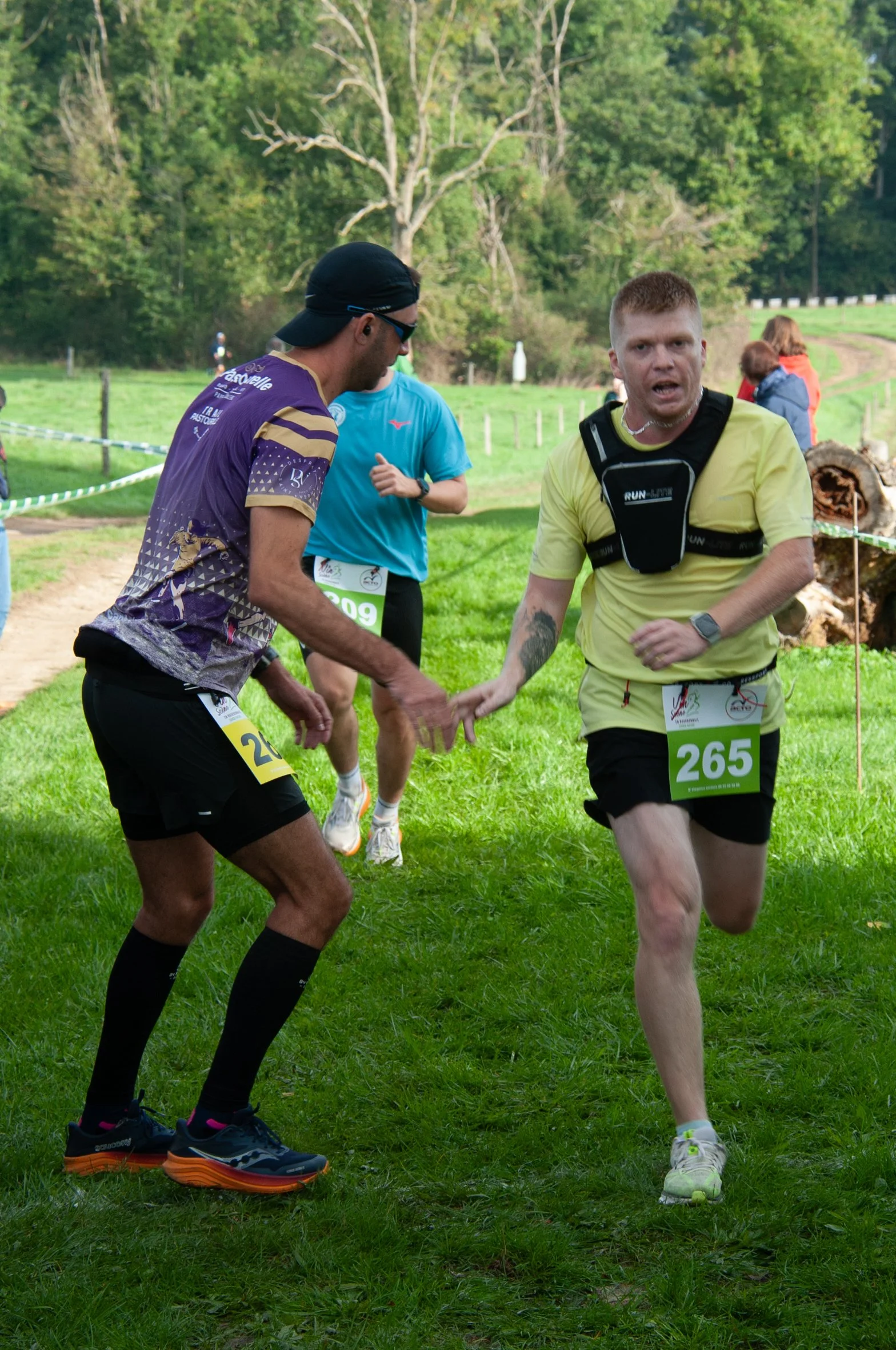 Deux coureurs se donnent la main pendant une course en plein air, avec un paysage verdoyant en arrière-plan.