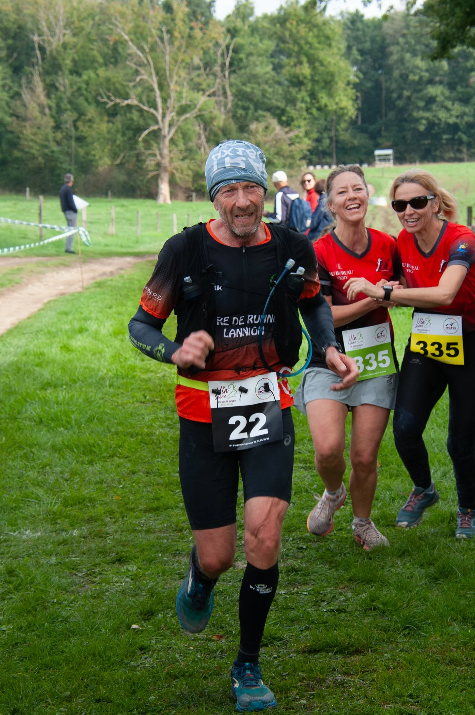 Des coureurs participant à une course dans un environnement naturel vert, certains souriants et en pleine étape.