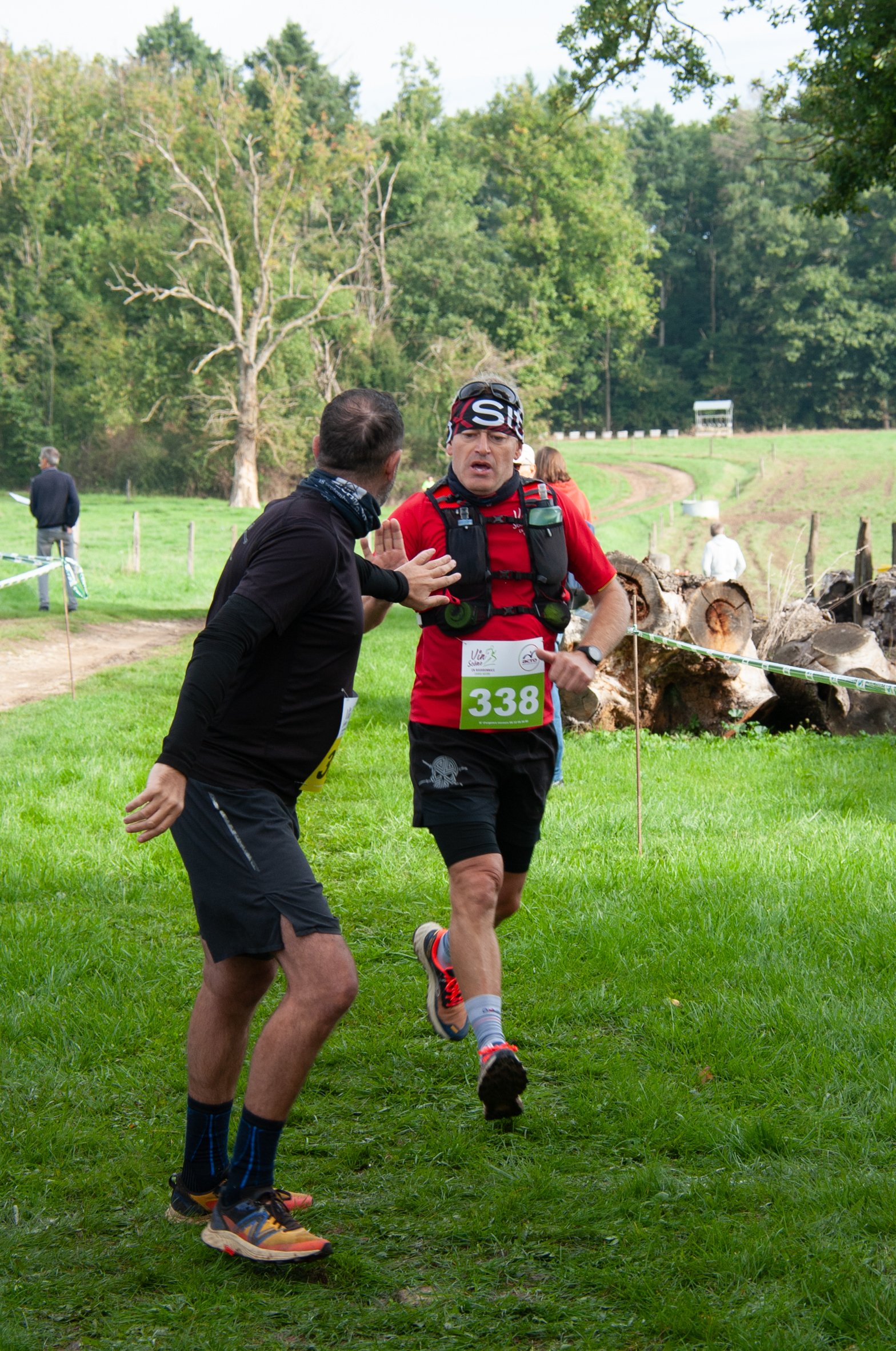 Un coureur participant à une course en course dans un parc, en train d'être encouragé par une personne qui parle avec lui, avec la nature en arrière-plan.