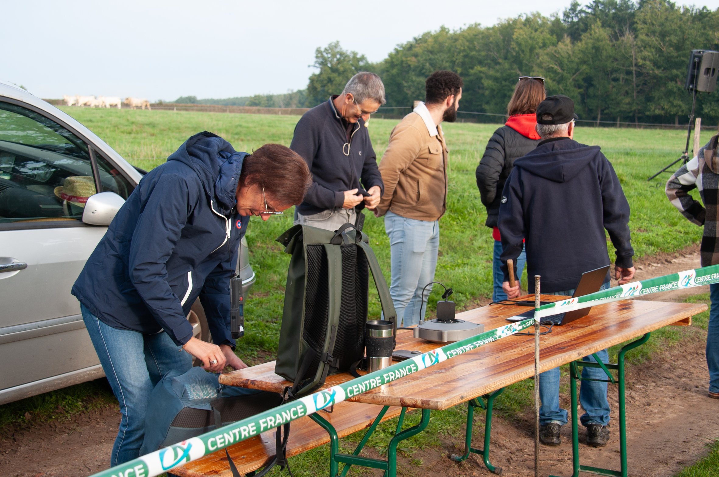 Groupe de personnes dans une ferme, installant du matériel pour une activité en plein air, avec un enclos ou une clôture barrée passant devant la table.