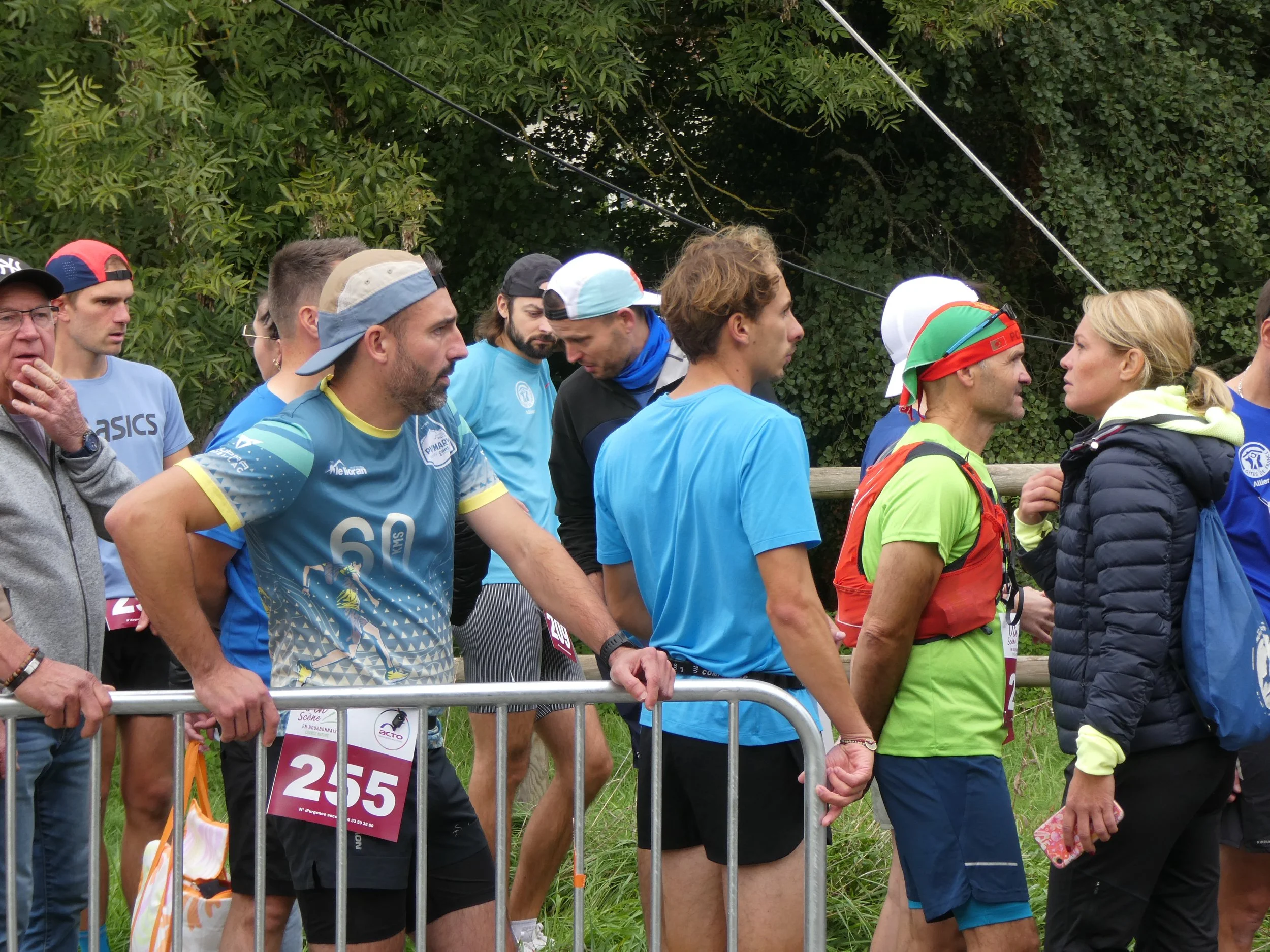 Groupe de coureurs de marathon ou course de trail derrière une barrière en attente au départ, en extérieur avec des arbres en arrière-plan