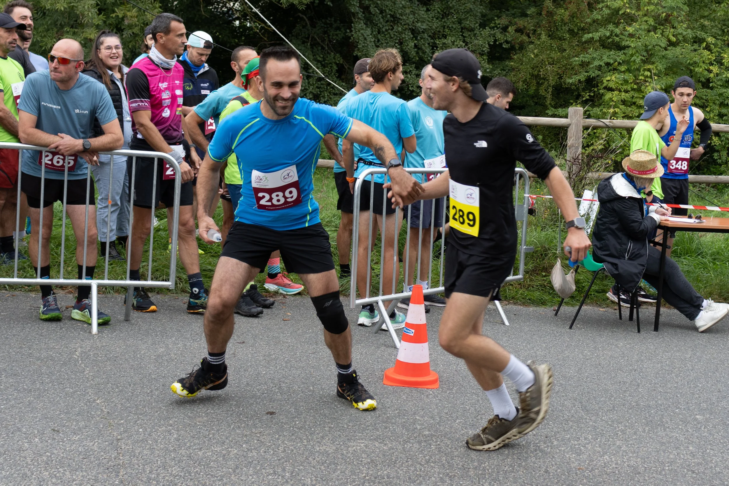Deux coureurs de marathon se donnent la main à la ligne d'arrivée, entourés d'autres participants et spectateurs.