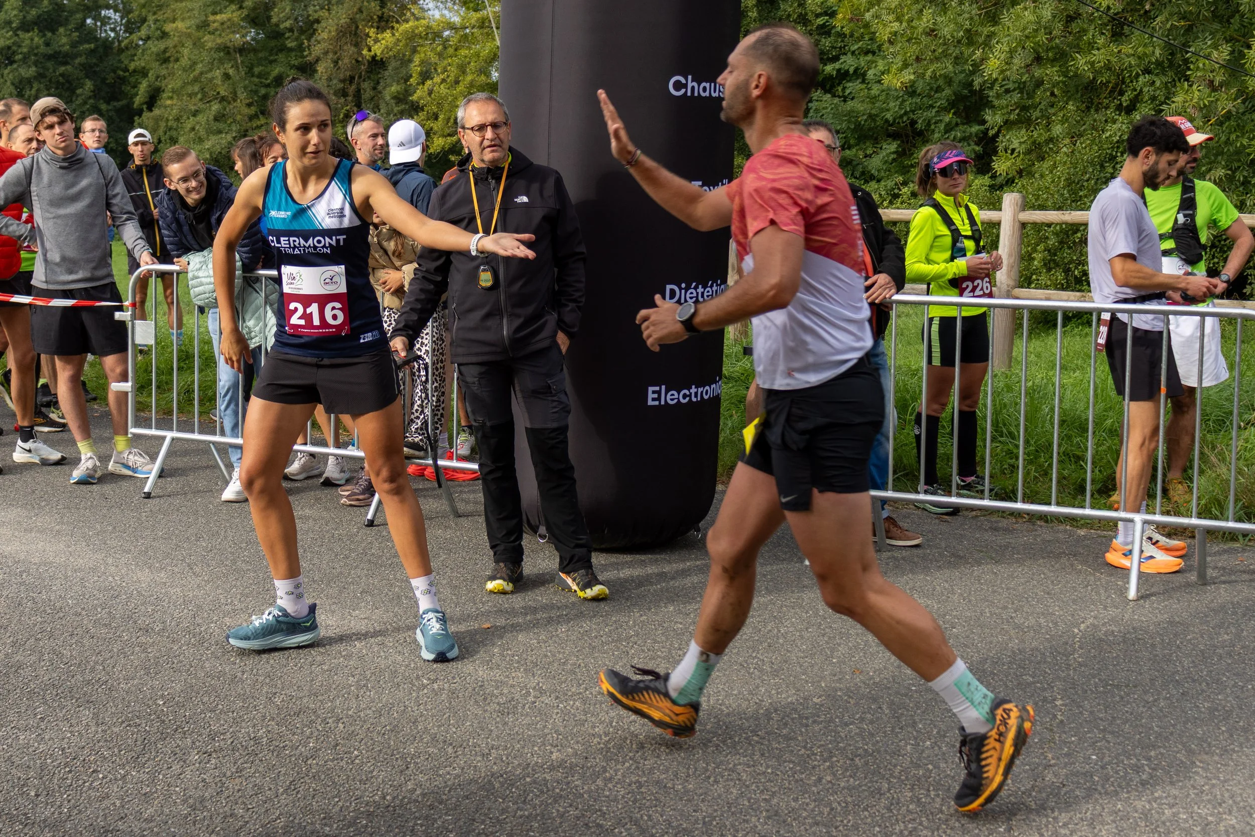 Un athlète en train de courir et un officiel lui donnant un signe de départ ou de fin de course lors d'une compétition de course à pied, avec plusieurs spectateurs en arrière-plan.