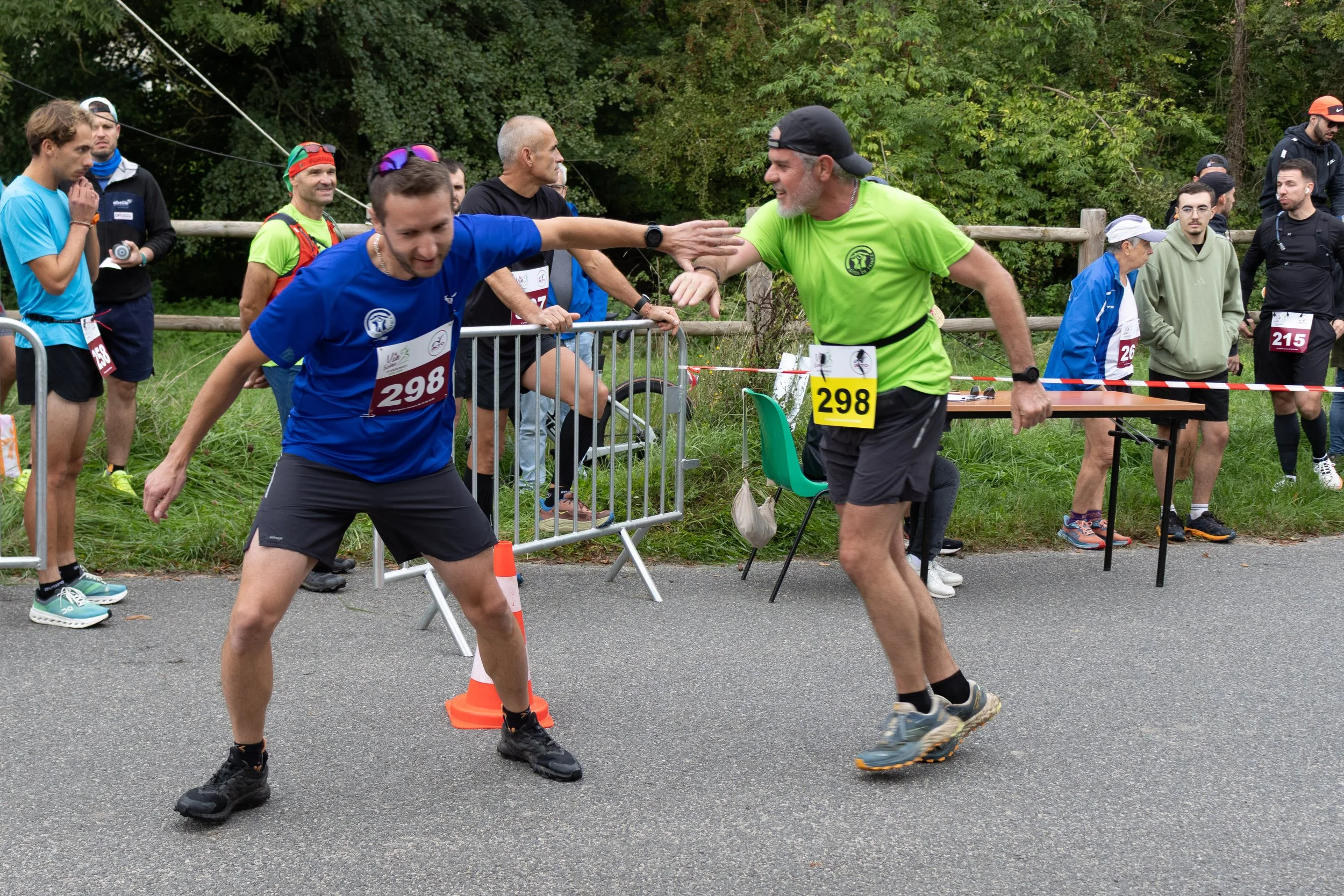 Deux coureurs se donnent une poignée de main à la ligne d'arrivée d'une course, entourés d'autres participants et spectateurs.