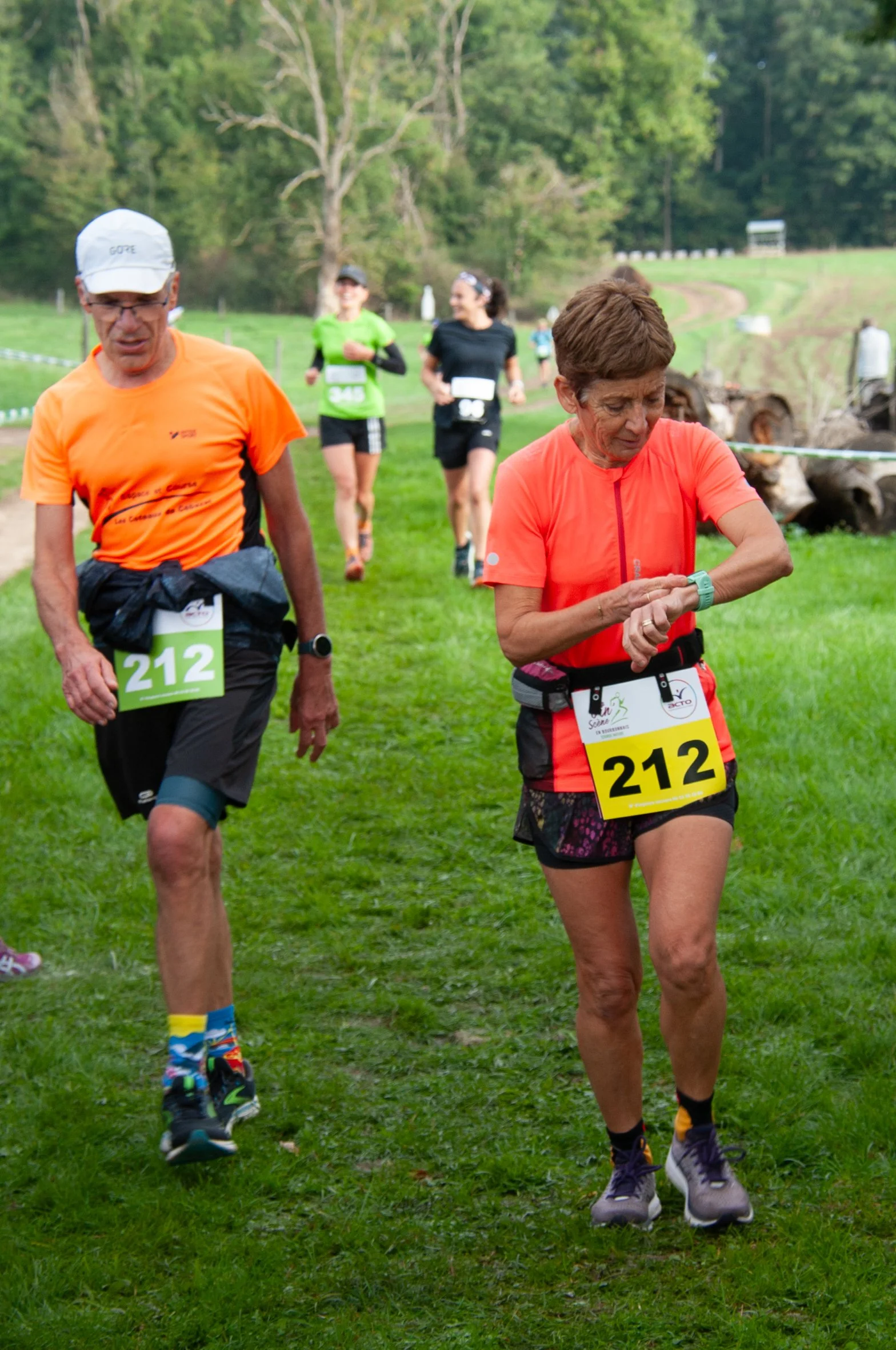 Des coureurs participant à une course en plein air, portant des numéros d'identification, dans un environnement vert avec des arbres en arrière-plan.