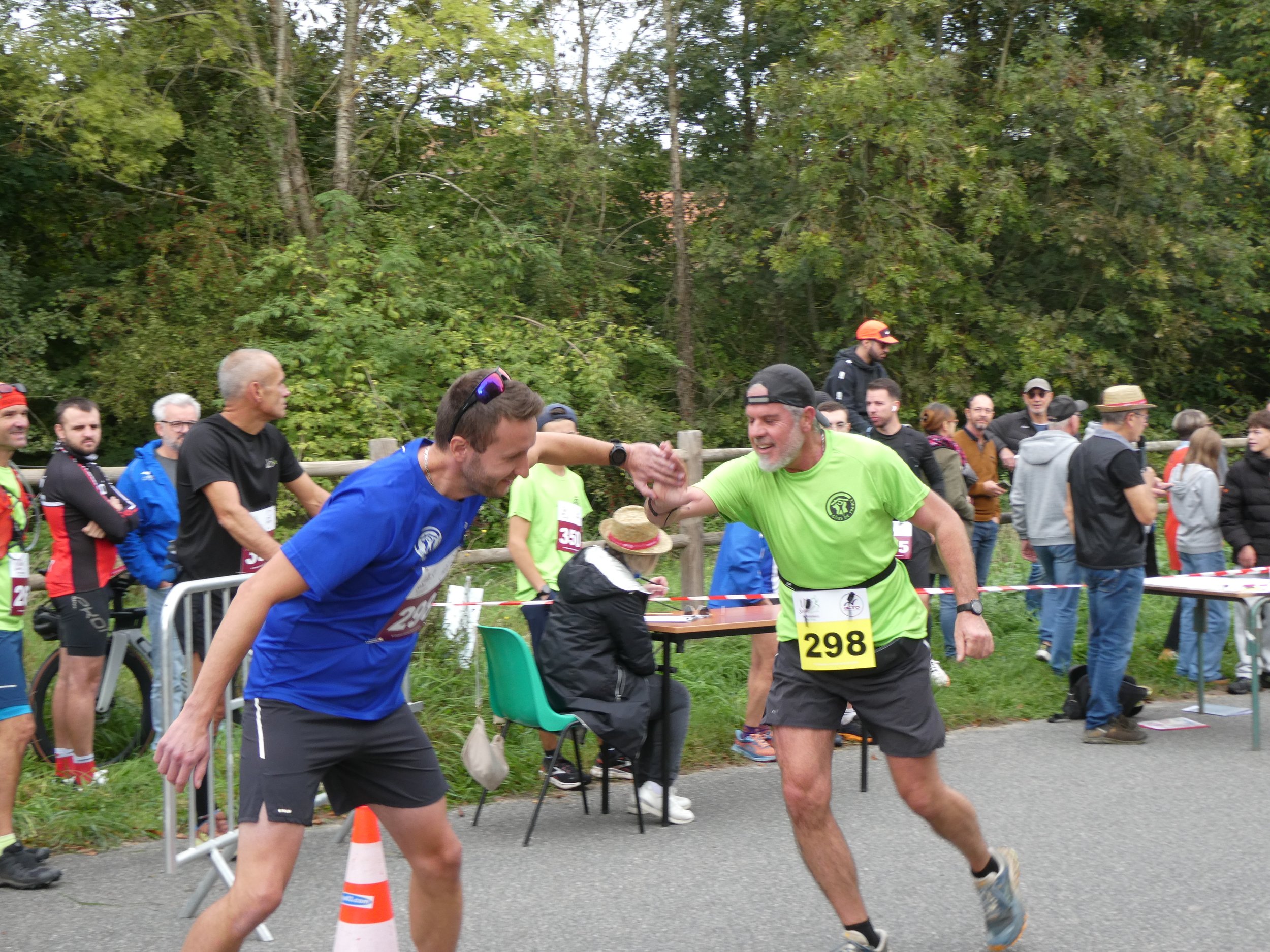 Deux coureurs se congratulent après une course, entourés par un groupe de spectateurs et bénévoles.