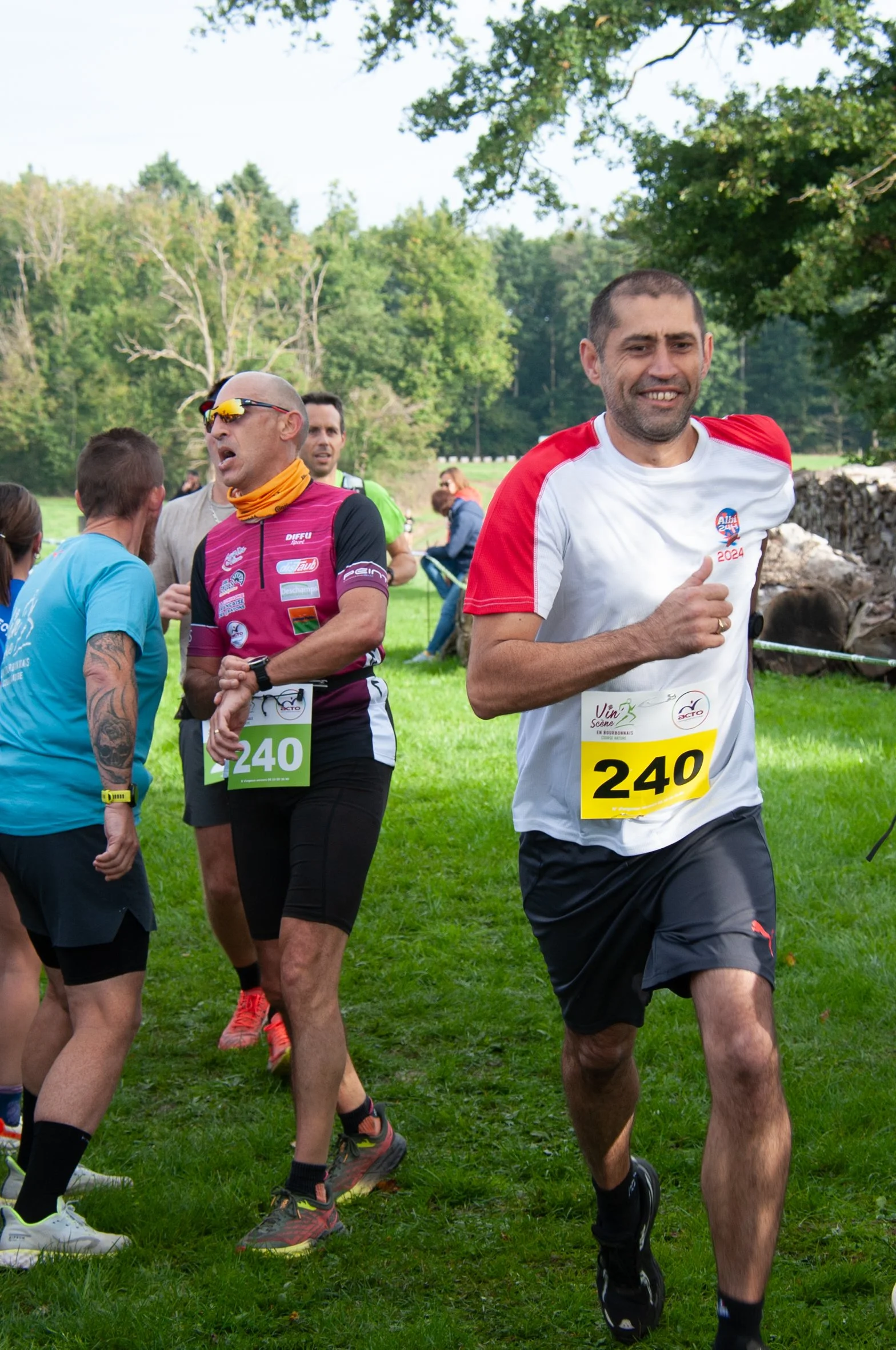 Des coureurs participent à une course en plein air, portant des numéros 240 et autres, avec un paysage verdoyant en arrière-plan.