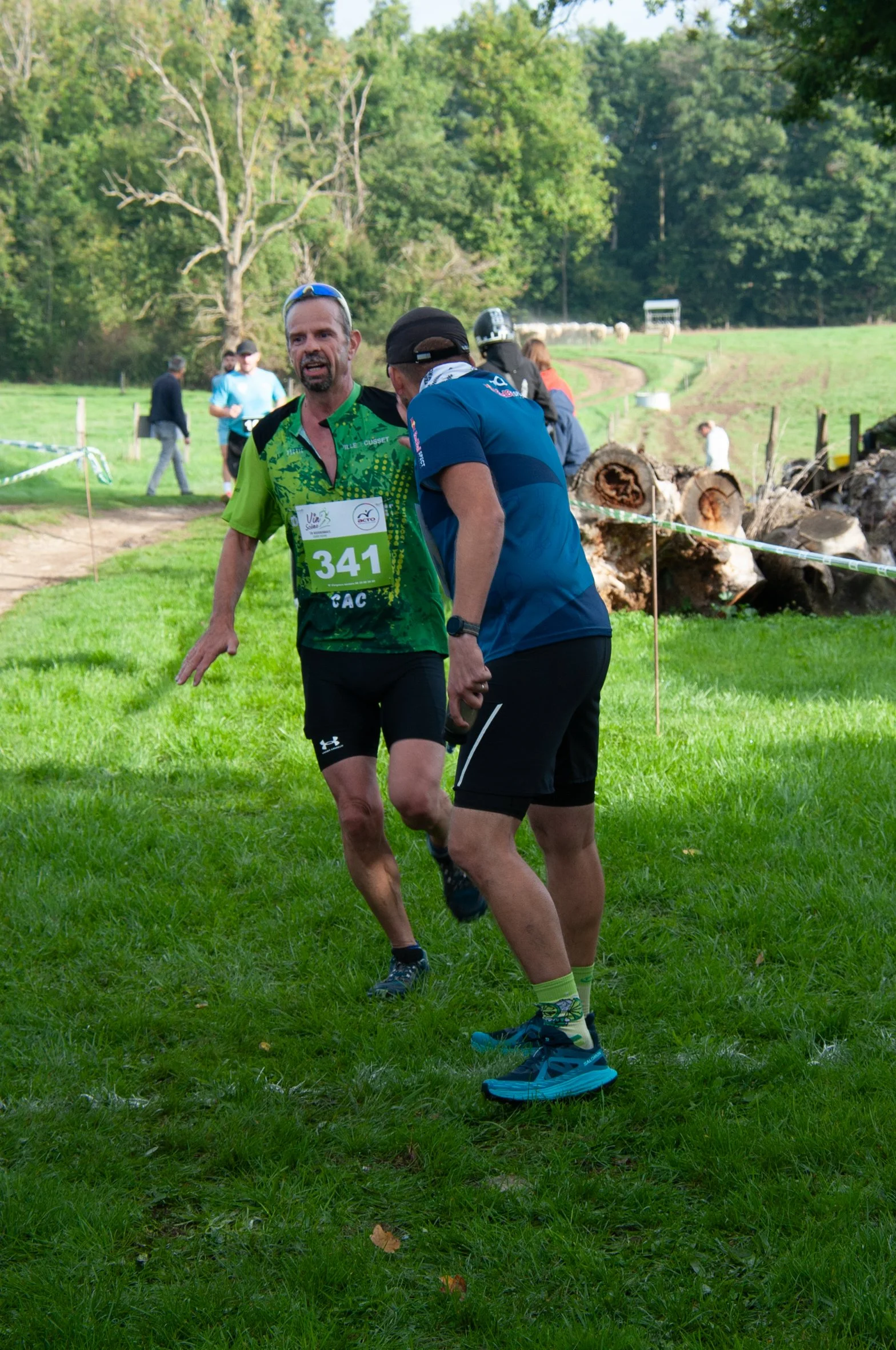 Deux hommes en vêtements de sport discutent lors d'une course ou un trail en pleine nature, avec des arbres et un chemin en background