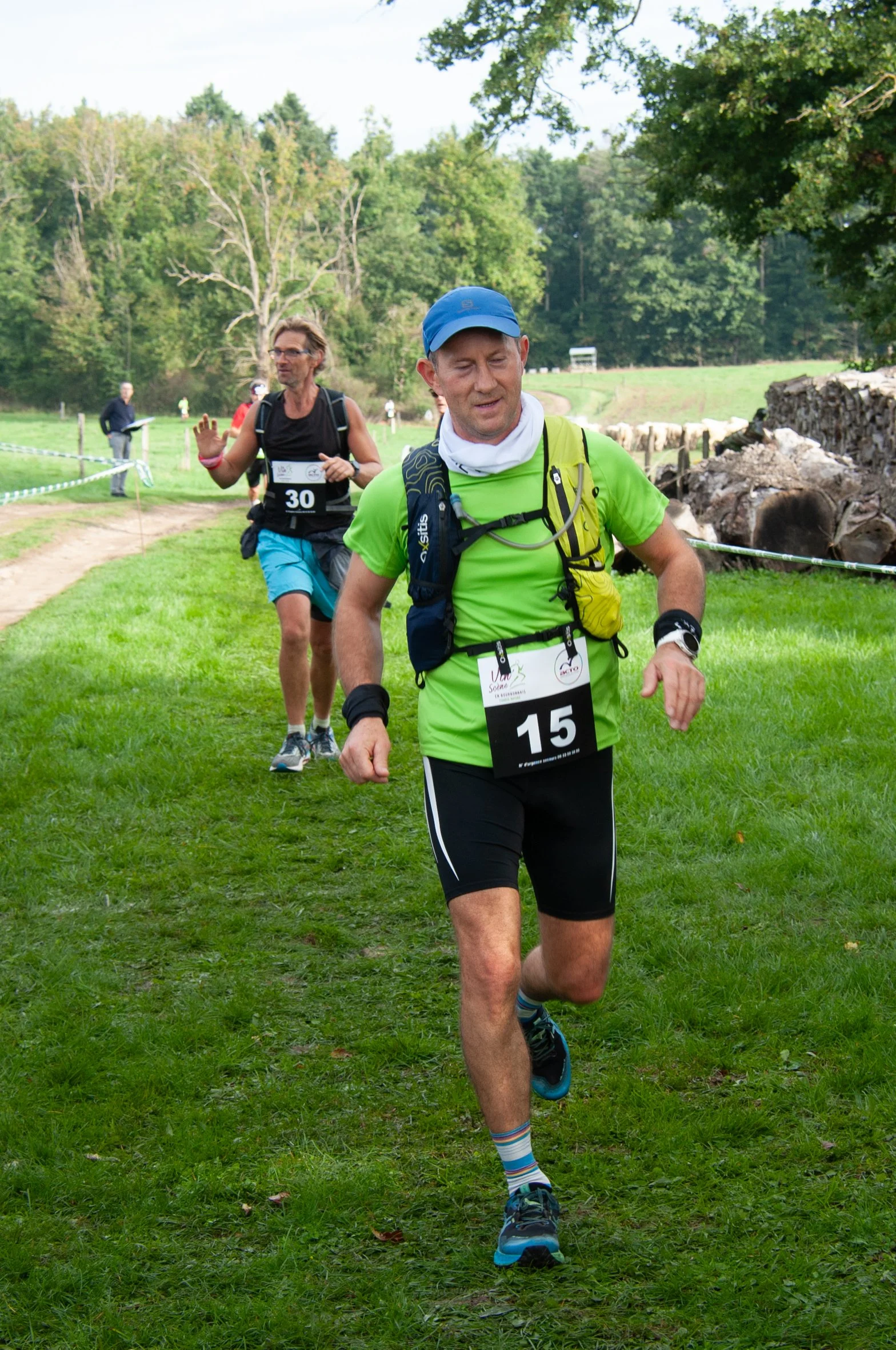 Deux coureurs participent à une course en plein air avec un paysage verdoyant, arbres et chemin en gravier.