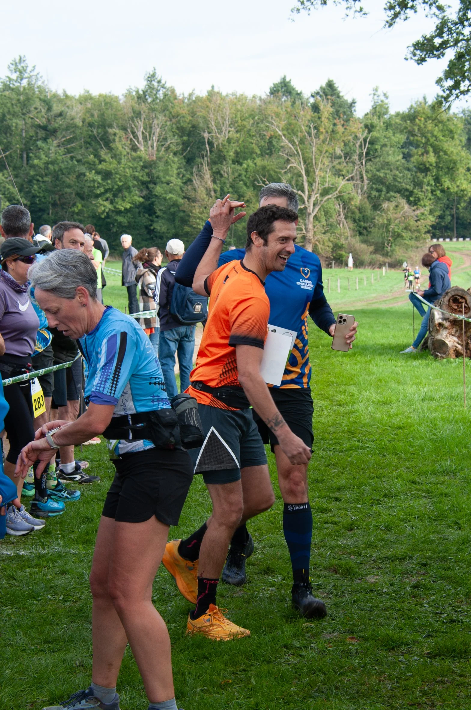Groupe de coureurs lors d'une course en plein air, entouré de spectateurs, avec un paysage verdoyant en arrière-plan.