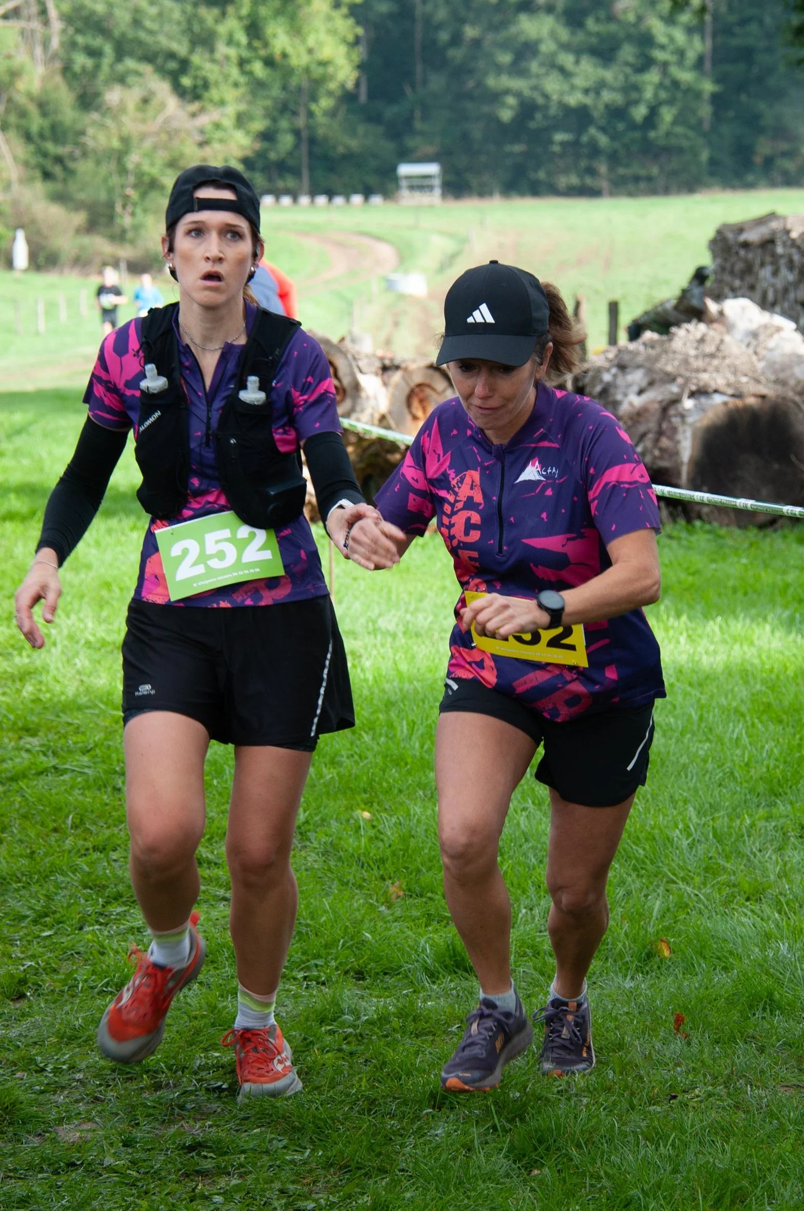 Deux femmes courent lors d'une course en pleine nature, l'une d'elles semble avoir besoin d'aide et est soutenue par l'autre.