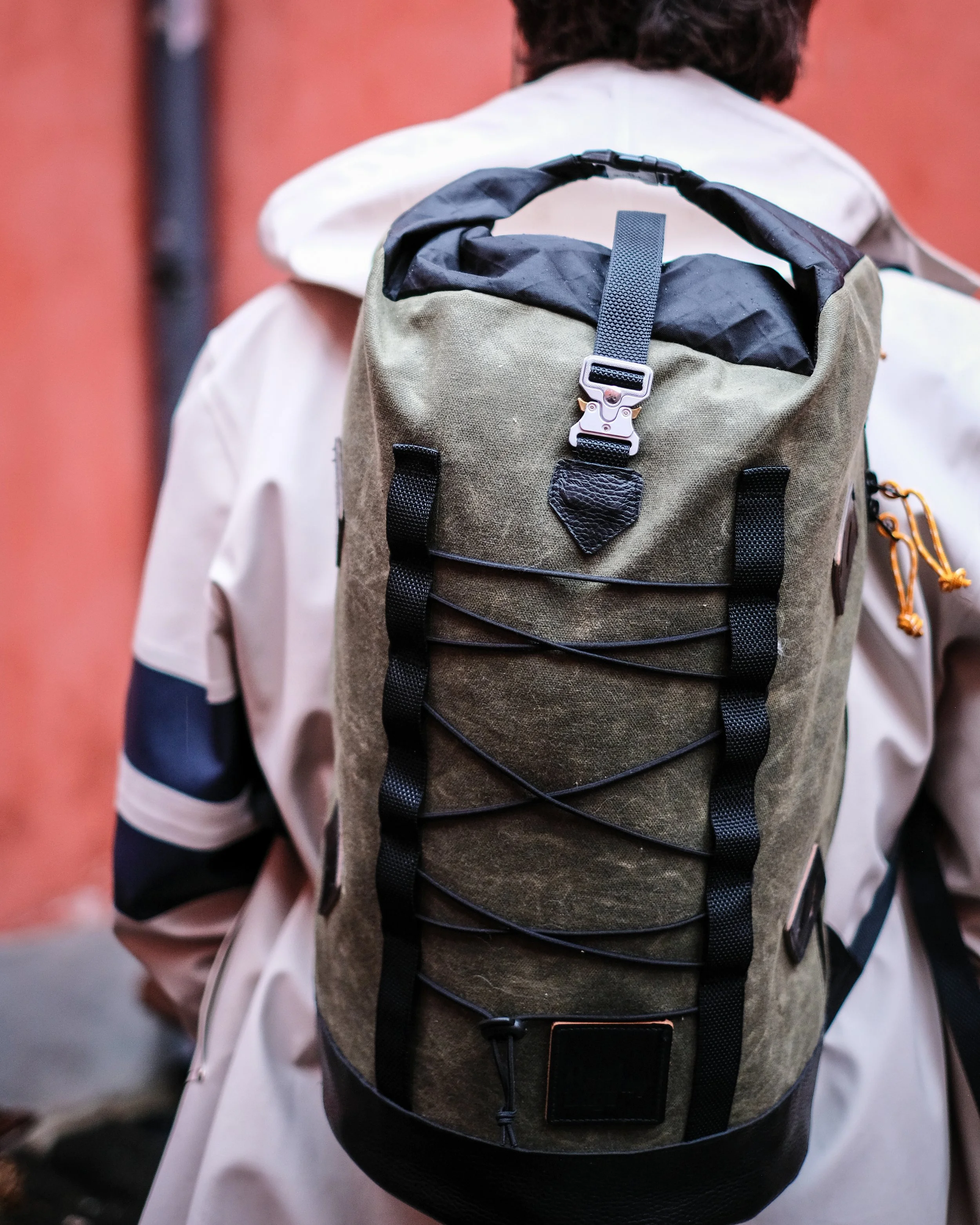 A person wearing a beige jacket and carrying a green and black backpack.
