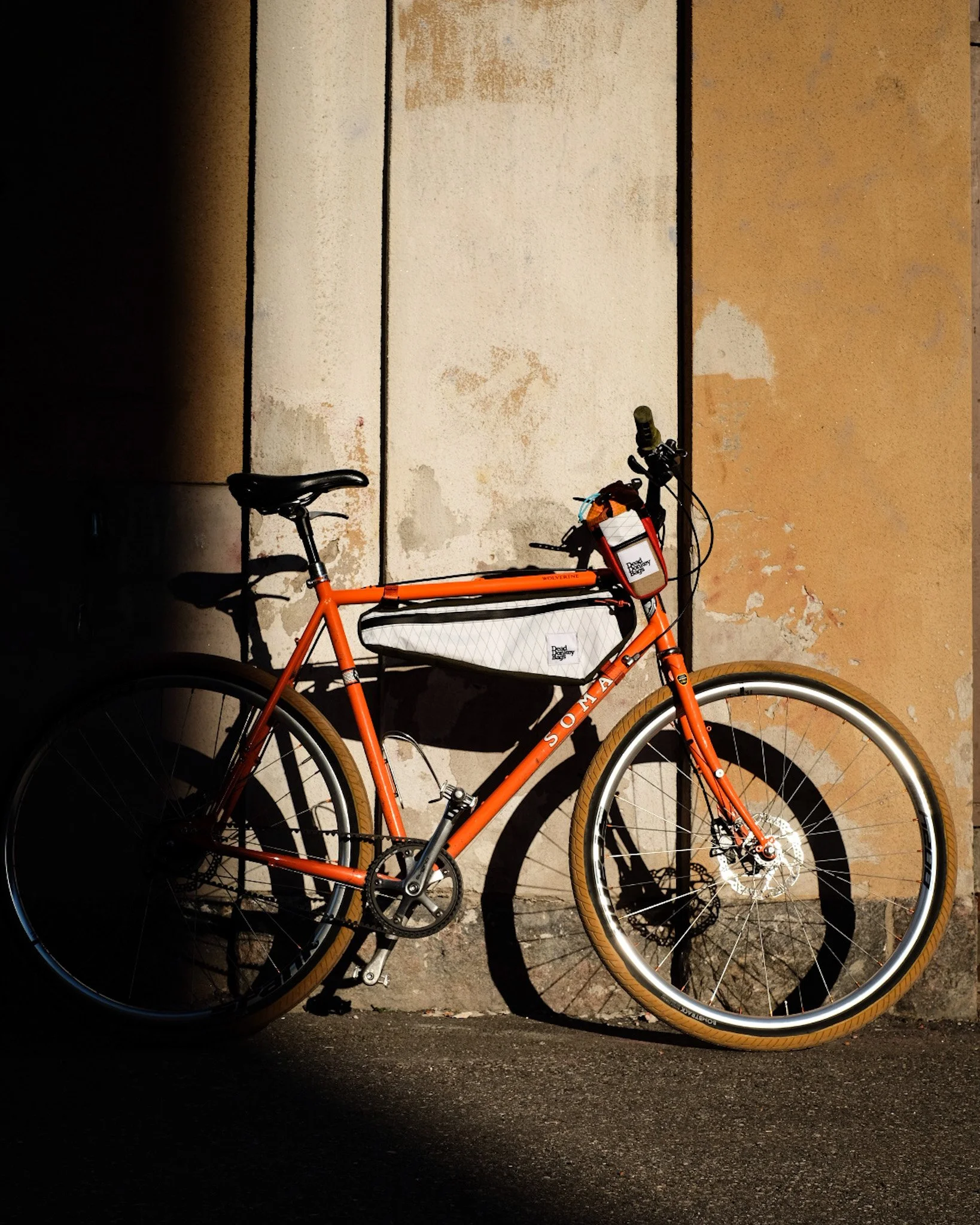 An orange bicycle leaning against a wall with peeling paint, casting shadows in sunlight.