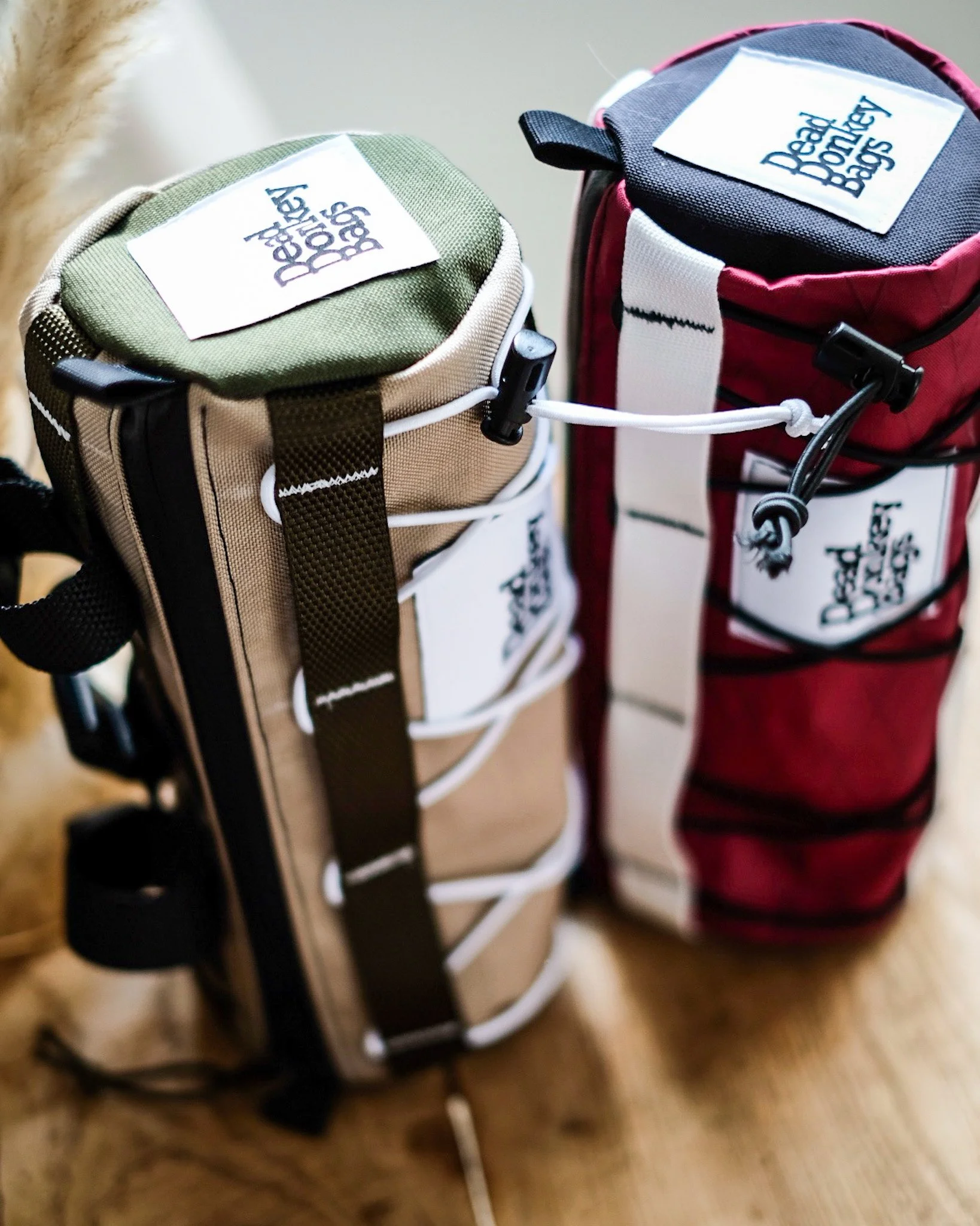 Two golf bags, one beige and green and the other red and black, standing upright on a wooden floor with the brand name 'Deadly Birdie Bags' displayed on tags.