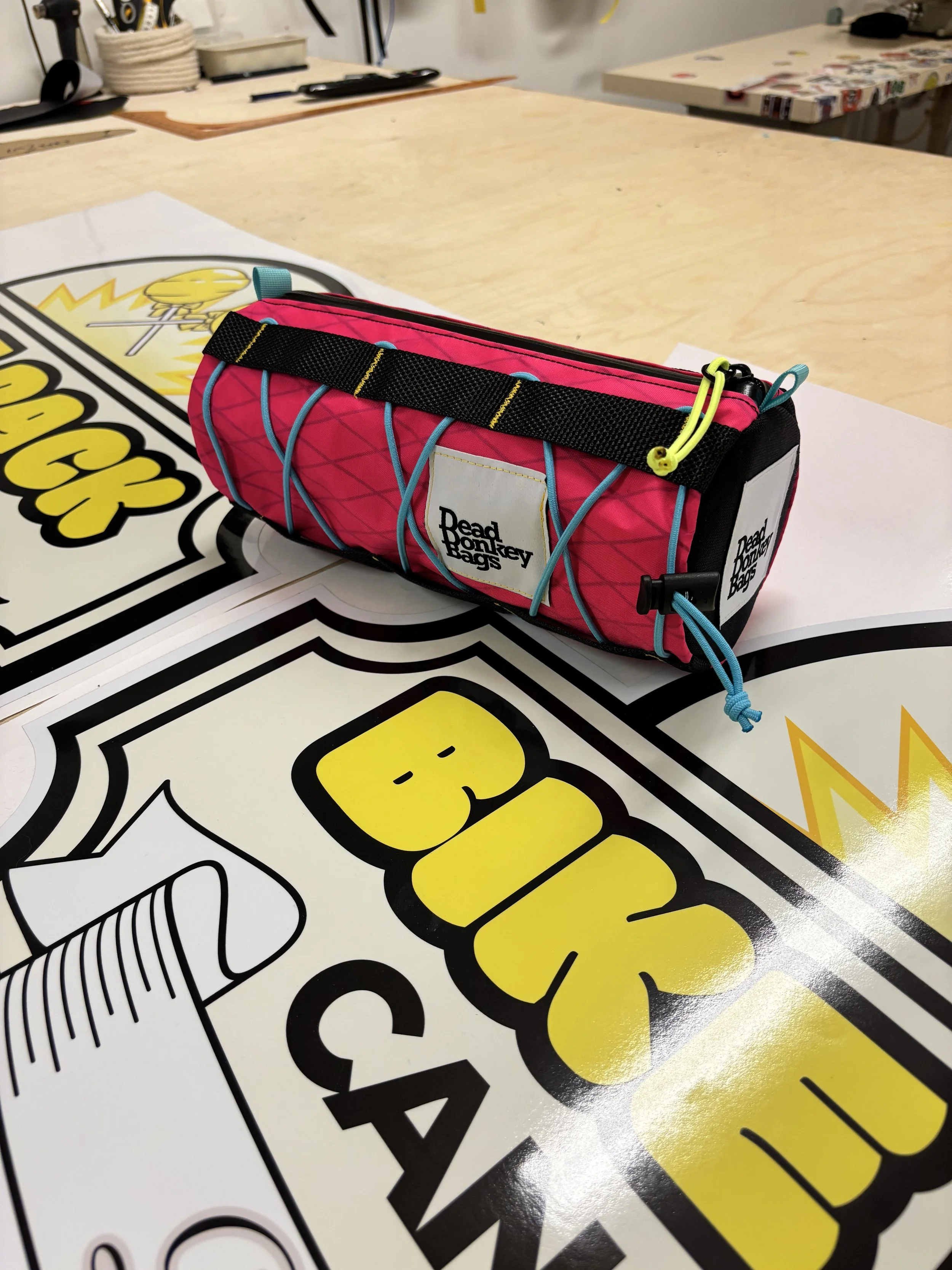 A pink and black Bead Monkey Bags pencil case with yellow, blue, and black accents, placed on a white surface with graphic stickers and a beige table in the background.