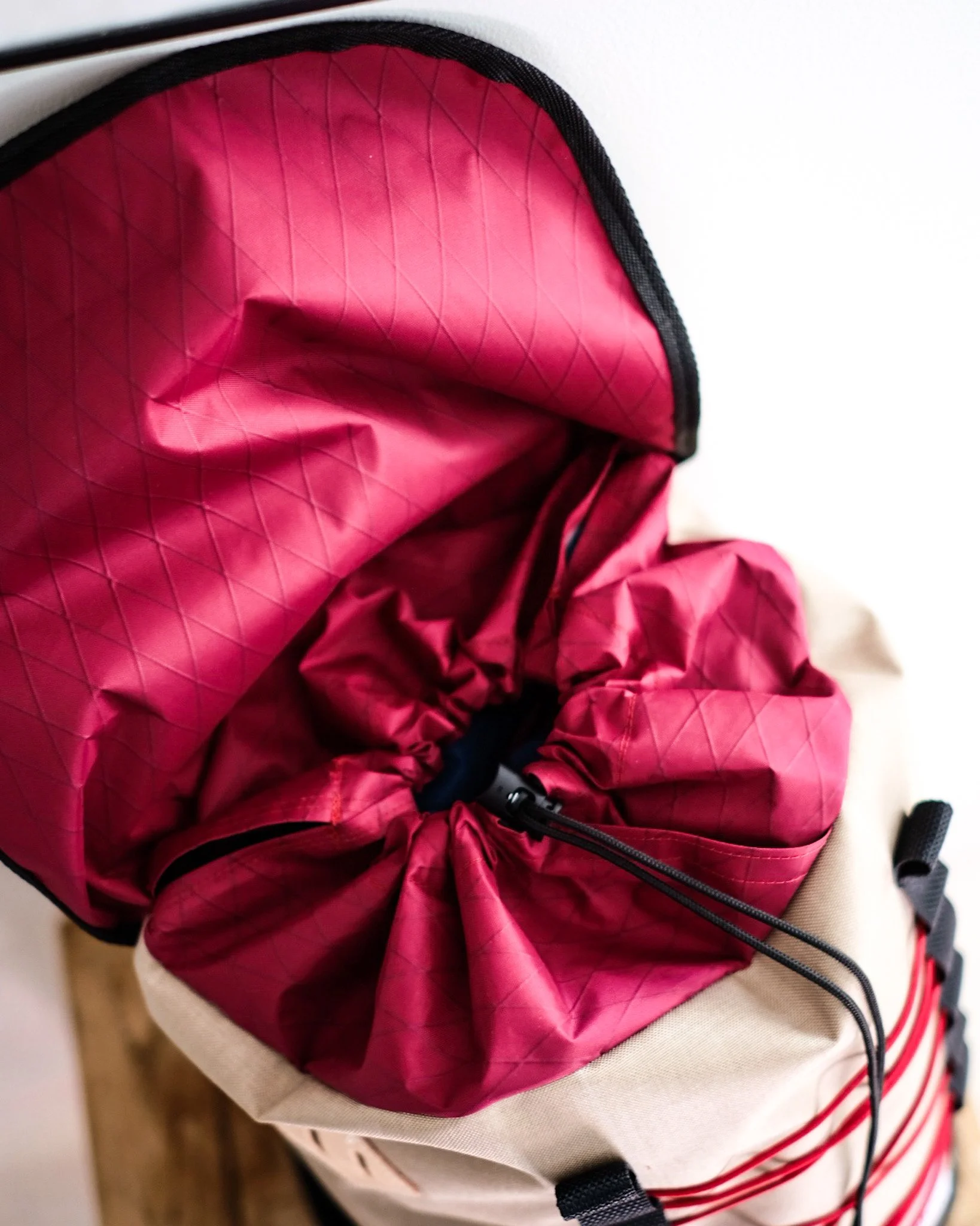 Open outdoor backpack showing red interior lining with diamond pattern, beige exterior with red stripes, and black zipper.