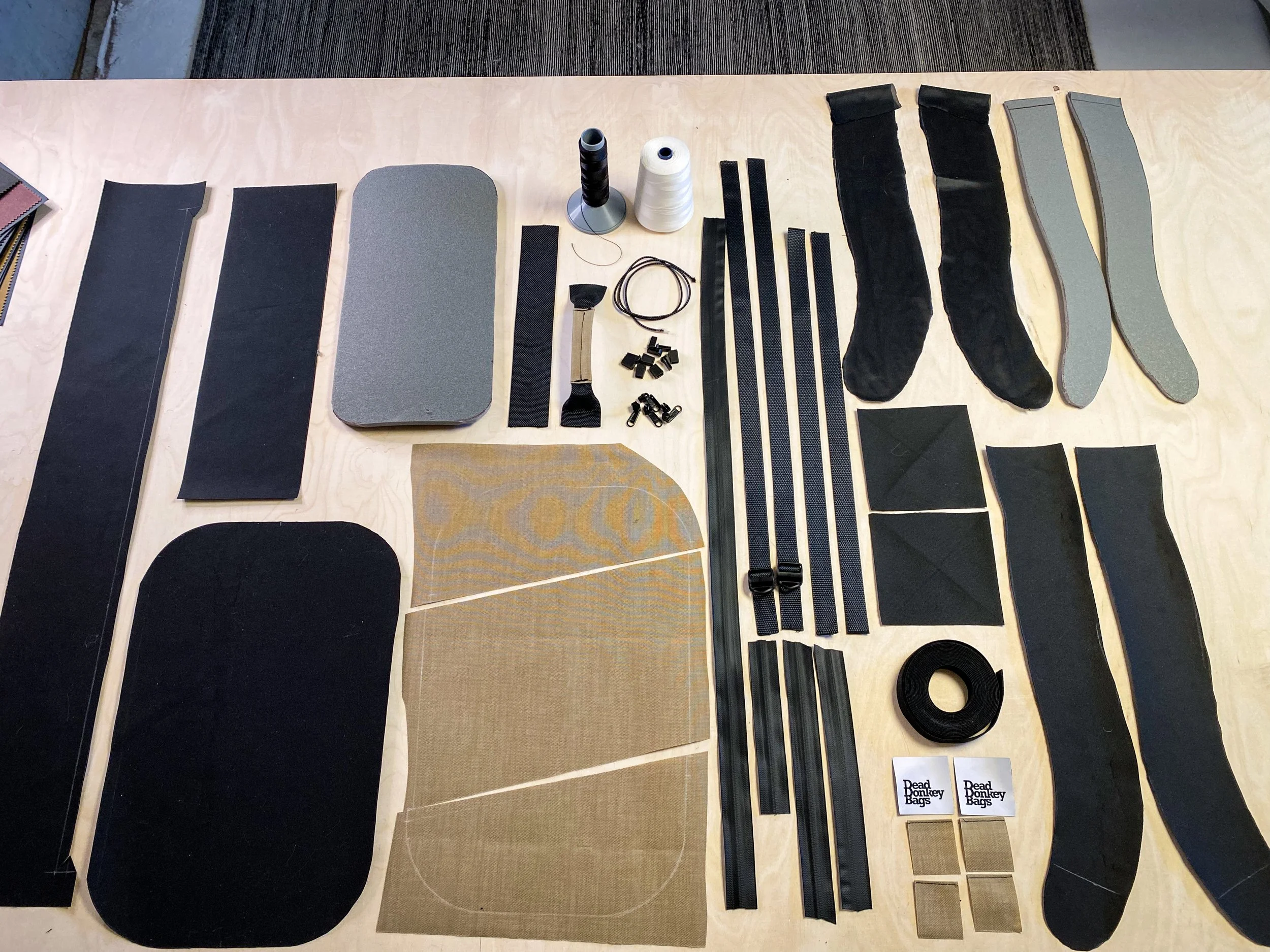 Disassembled parts and materials for a DIY project or craft, including fabric, straps, foam, tape, and small hardware pieces, laid out on a wooden table.