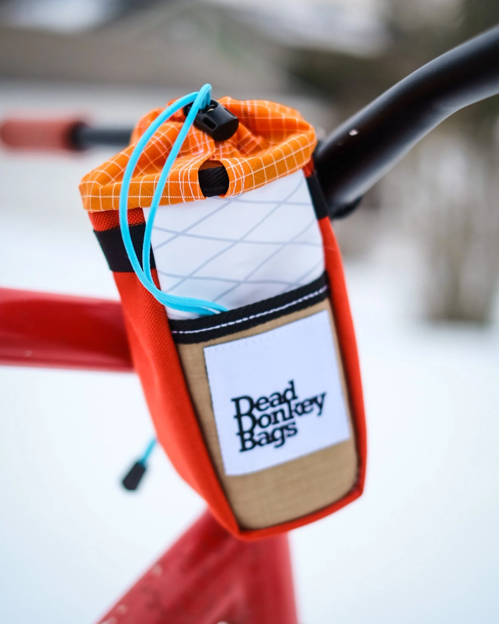 A red bike with a handlebar bag labeled "Dead Donkey Bags." The bag contains a white water bottle with an orange and grid pattern cover and a light blue tube.