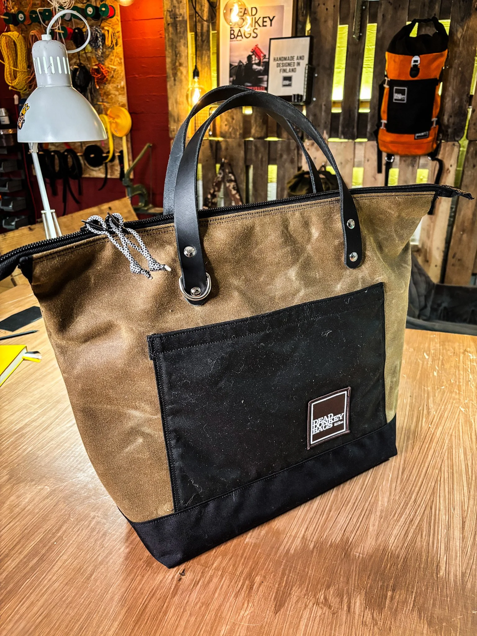 Brown and black Bradley Bags tote bag with handles on a wooden table in a rustic store setting.